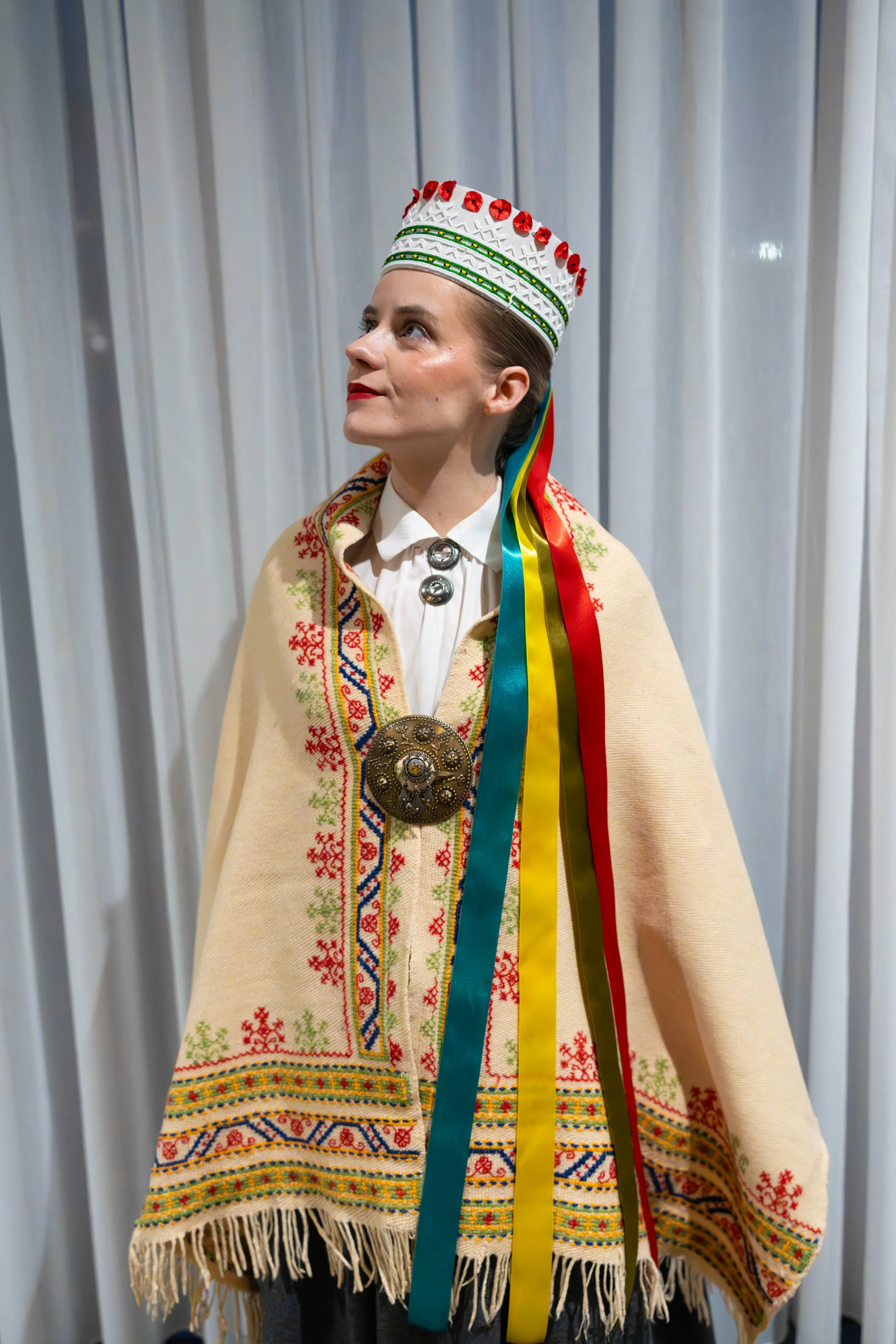 A woman wearing traditional Eastern European clothing, including a decorated shawl and a large embroidered headdress with ribbons.