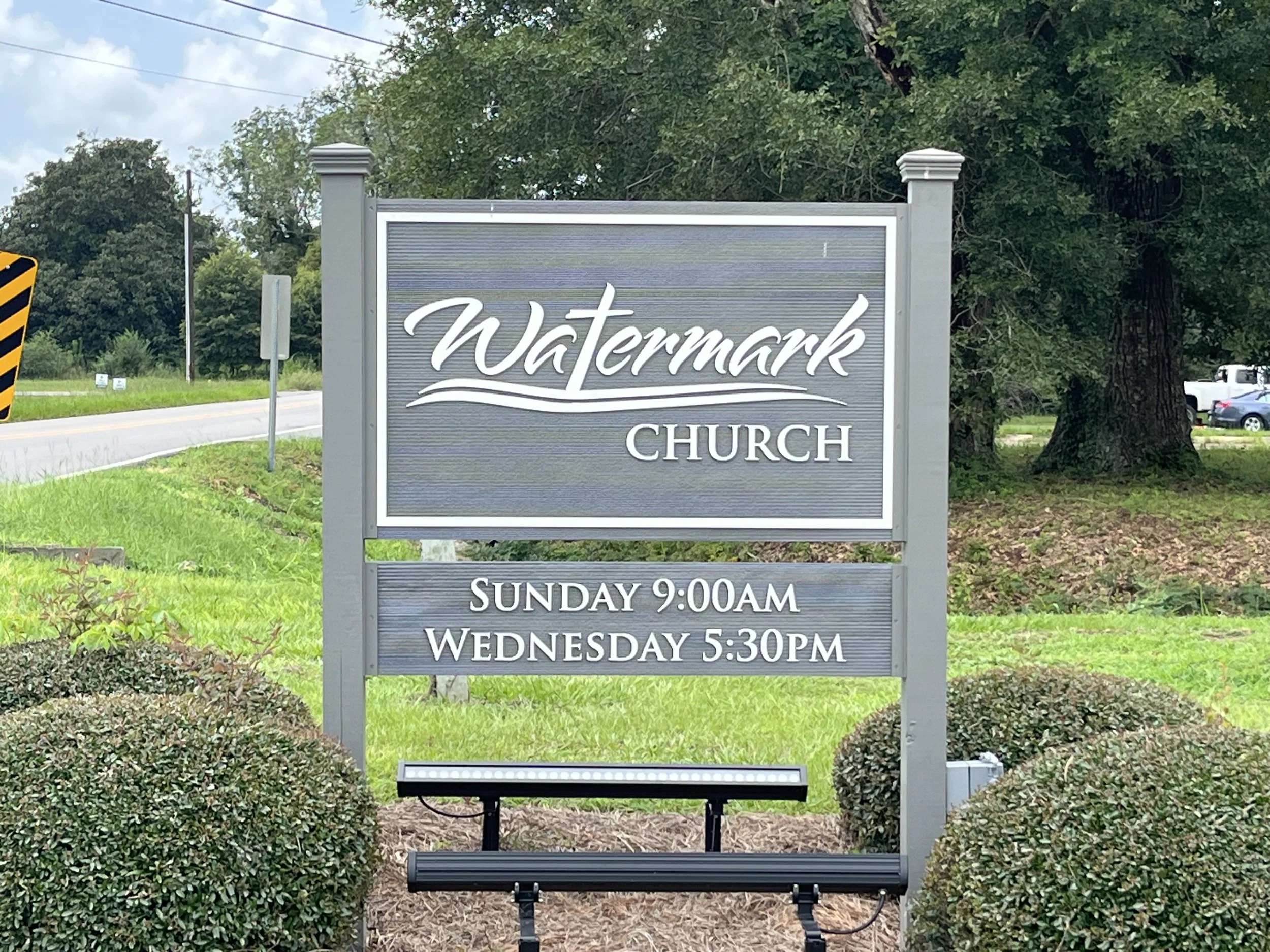 Sign for Watermark Church with service times listed, surrounded by greenery and trees.