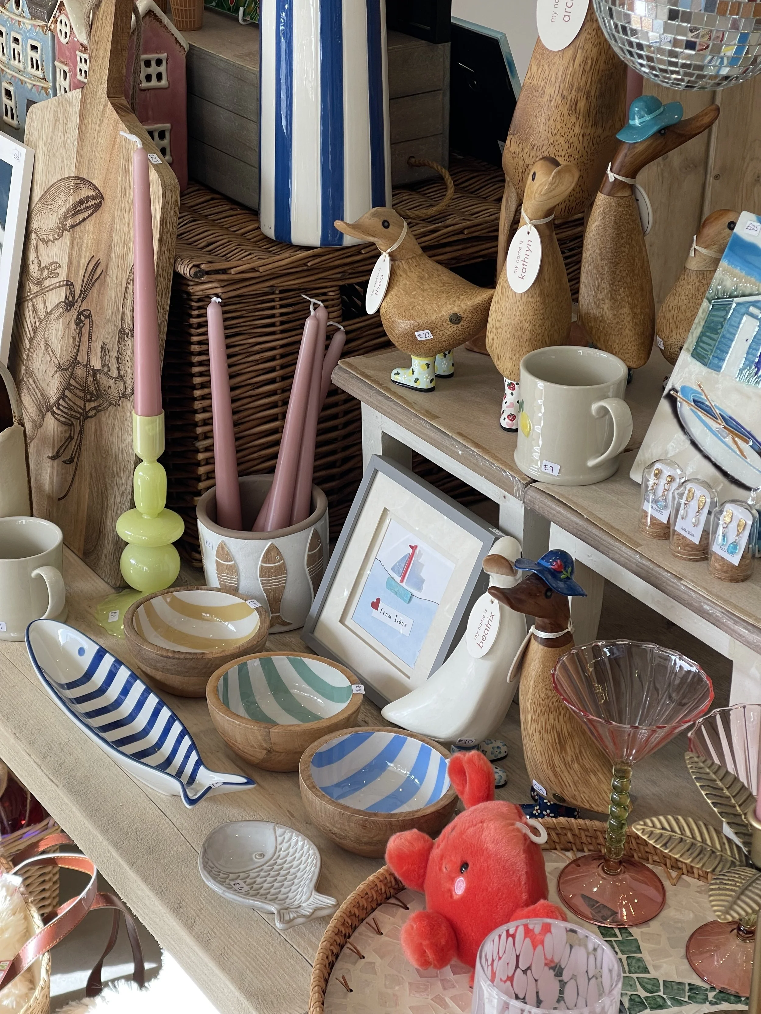 A giftshop display table of quirky home decor including wooden dcuk ducks, coastal stripe bowls, candlestick holders, ceramic dishes and bowls, and palm pals in a boutique giftshop in Looe, Cornwall.