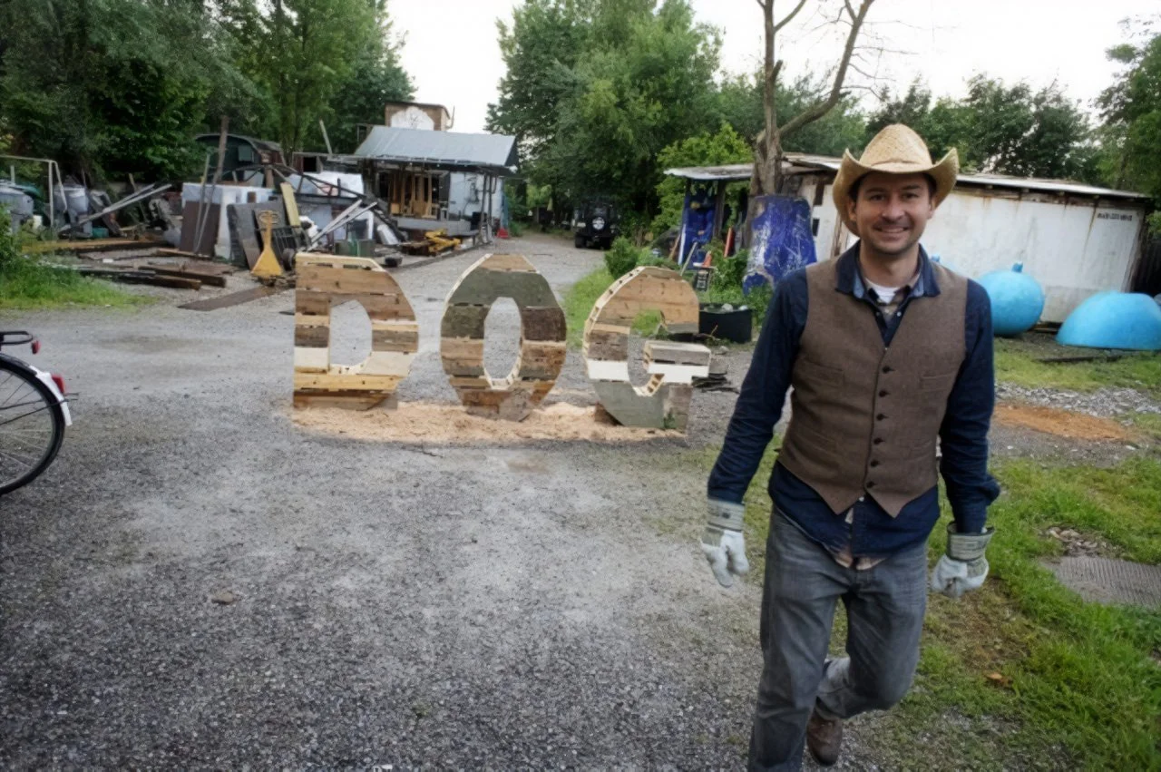 Art Title - Hotdog, Merlin Zuni, photo of Merlin Zuni in front of his sculptural art installation of large 3d letters DOG