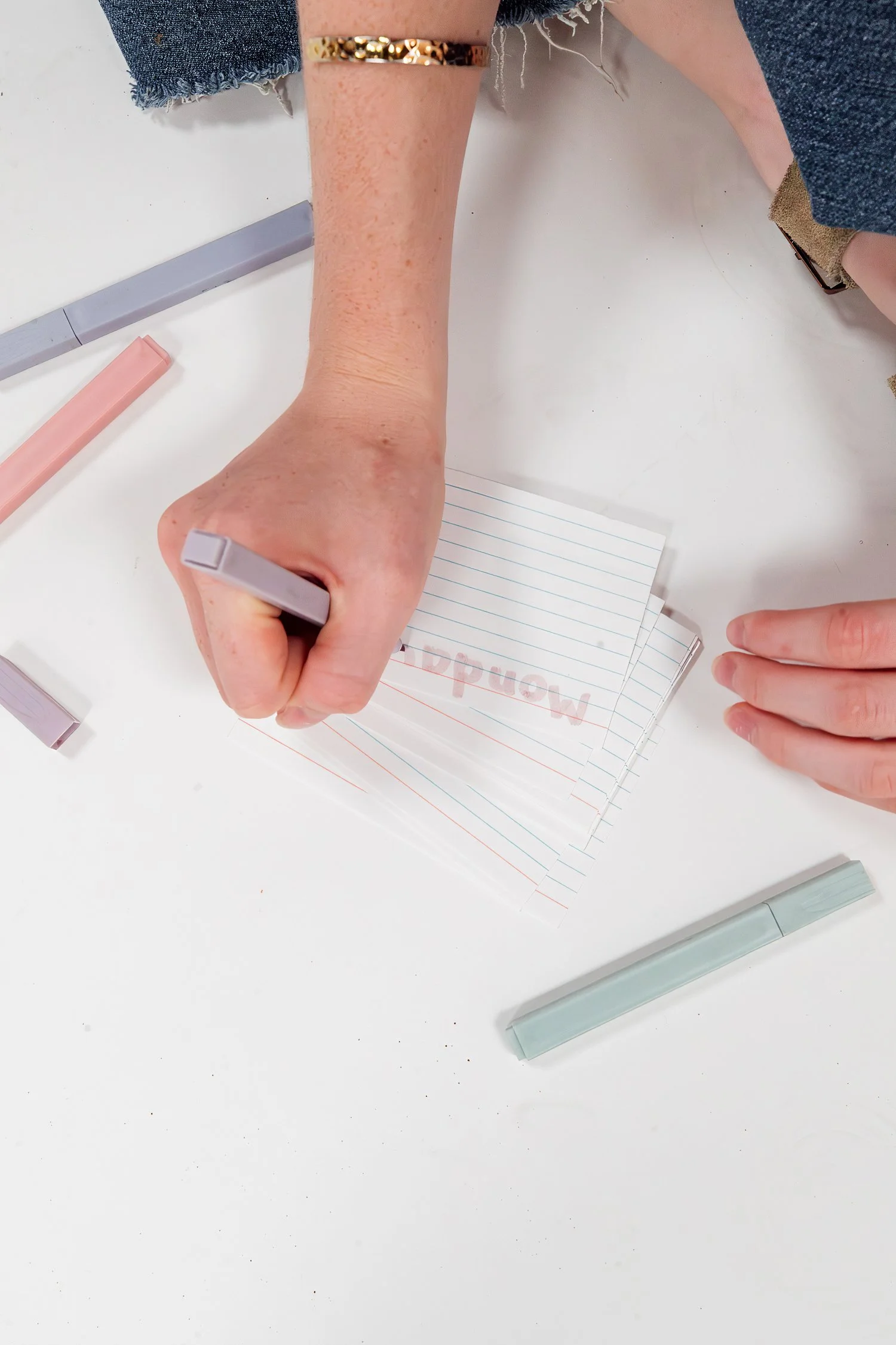 Adelyn writing a heading on lined study cards with pastel highlighters around her hands
