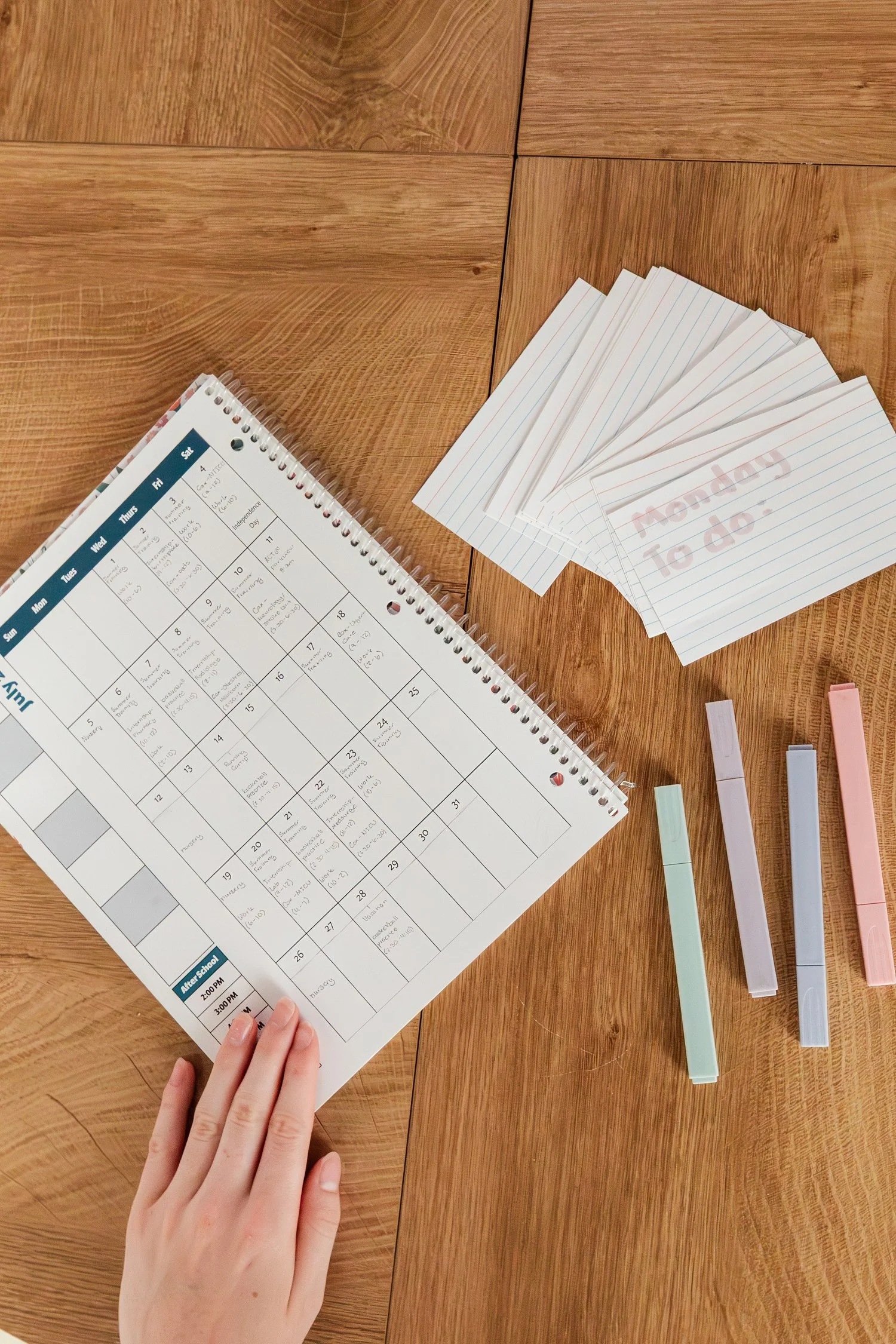 Paper study calendar, index cards, and pastel highlighters arranged on a wooden table