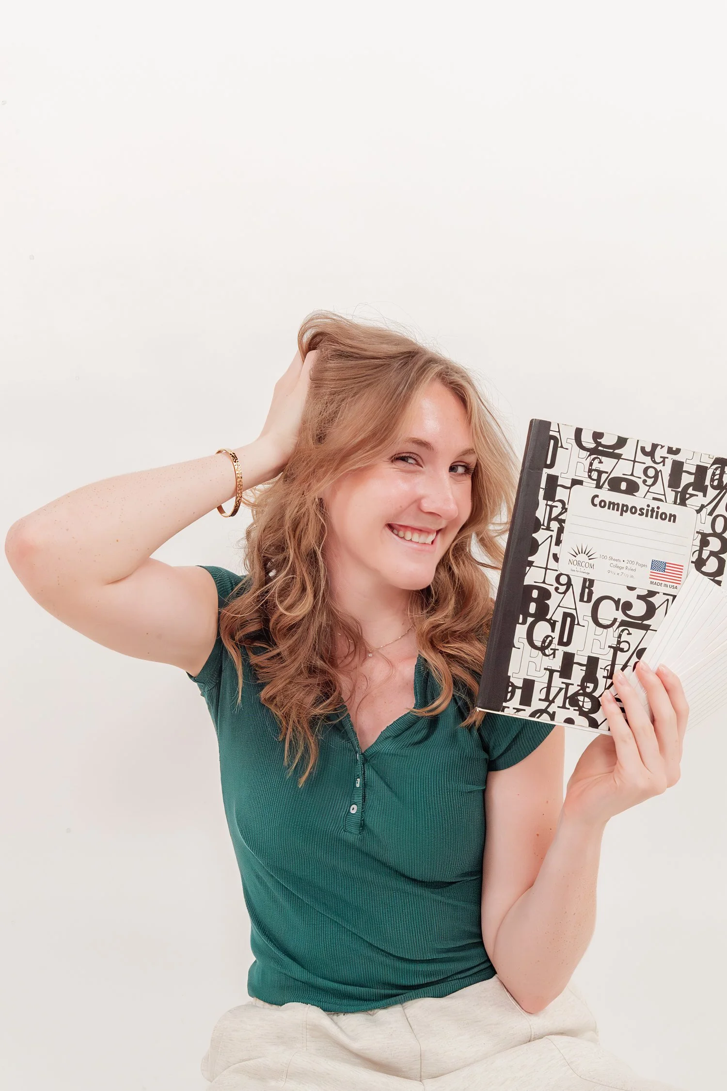Adelyn smiling with a composition notebook and a fan of index cards in the studio
