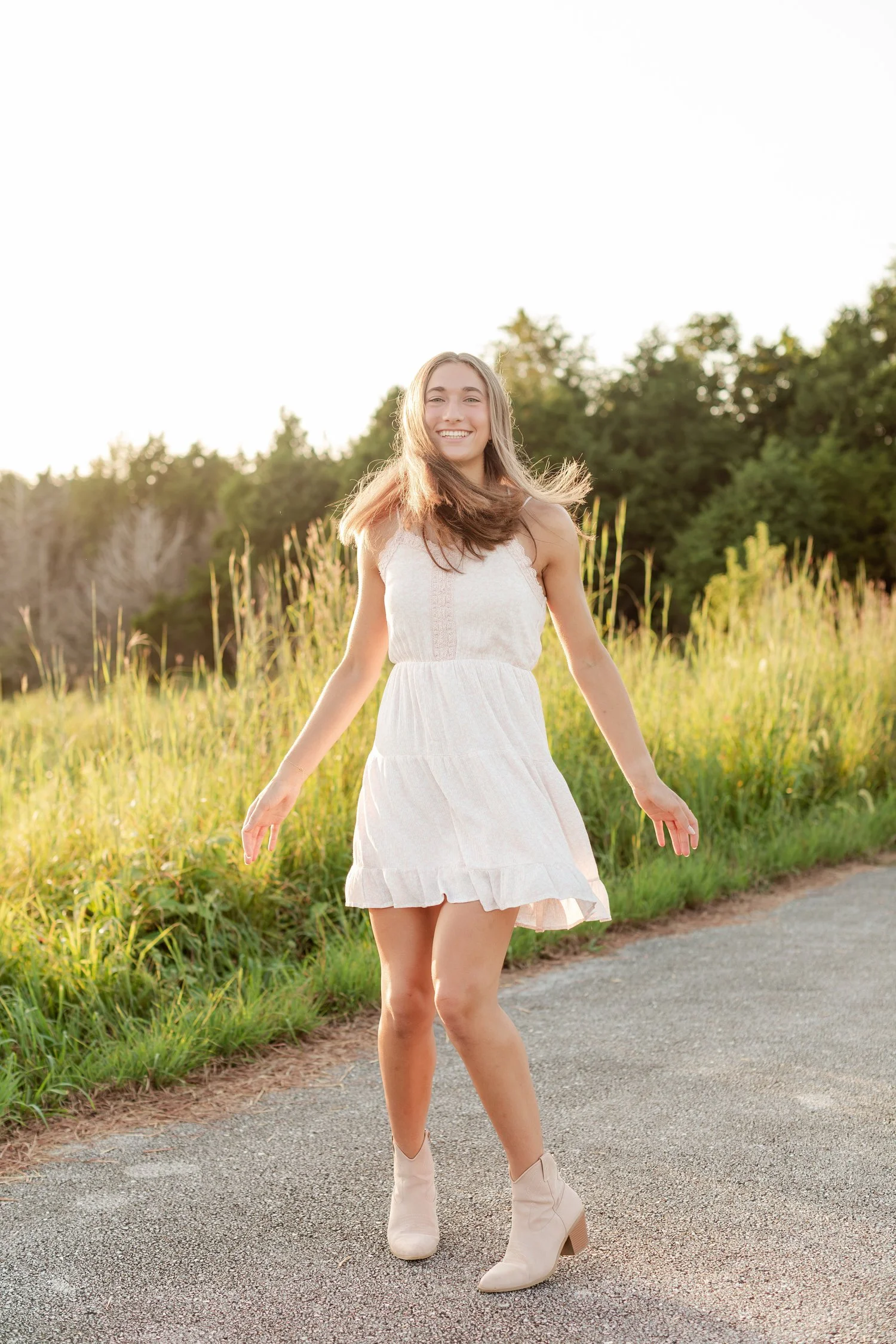 Young woman smiling toward the camera in a white dress outdoors.