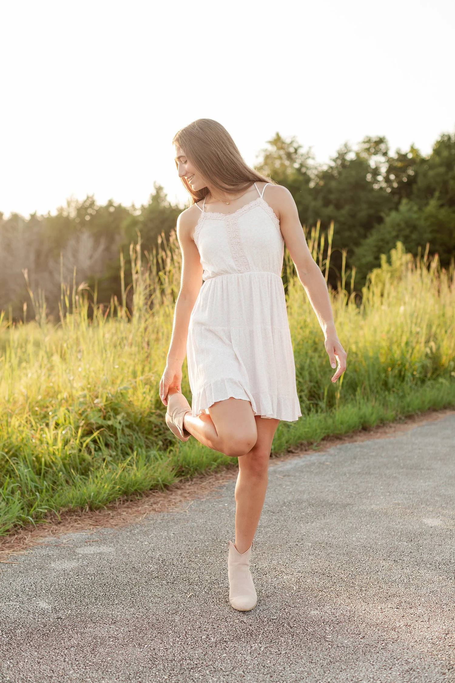 Young woman lifting one foot behind her in a white dress.