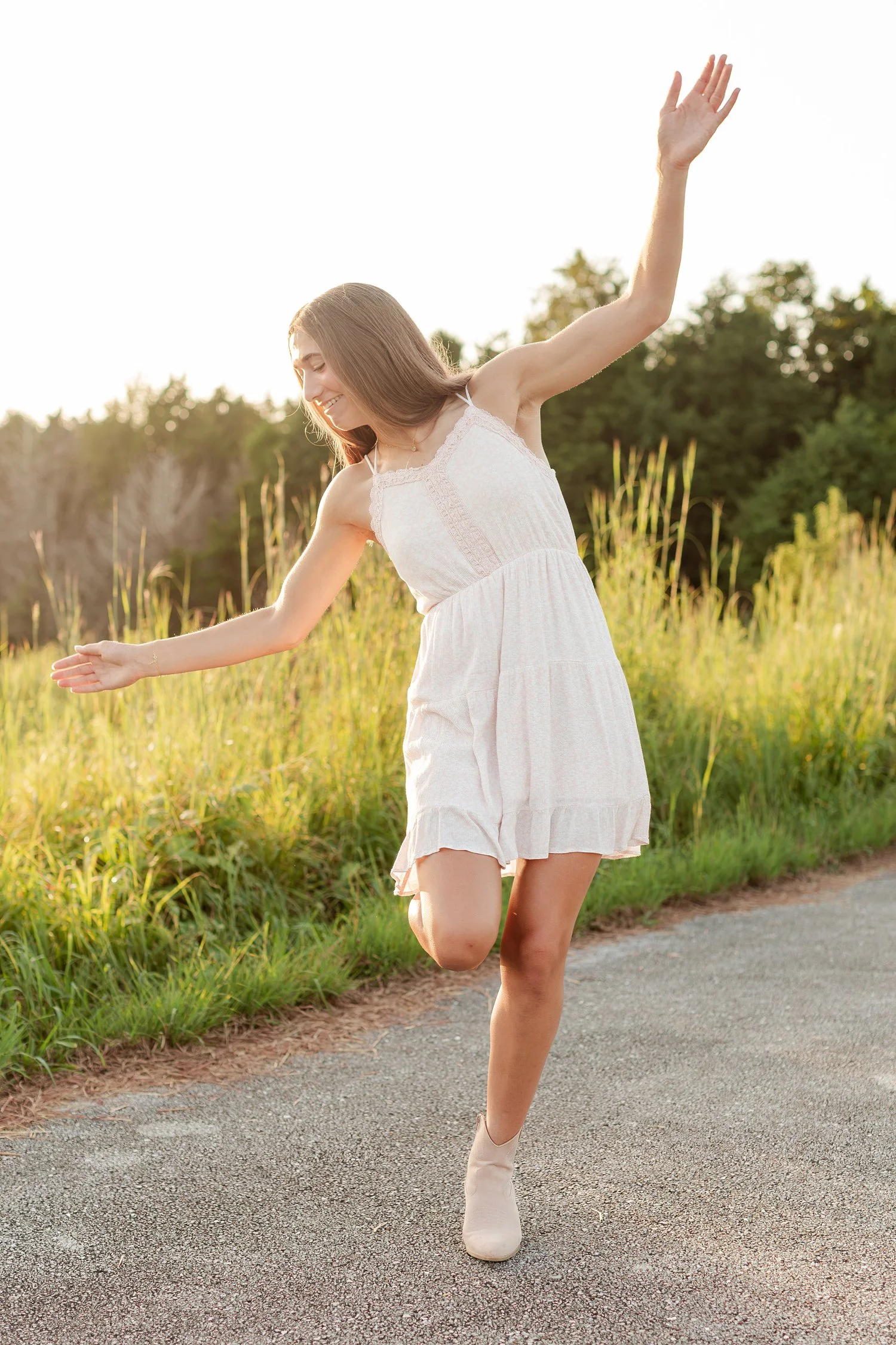 Young woman balancing with one arm raised beside a grassy field.