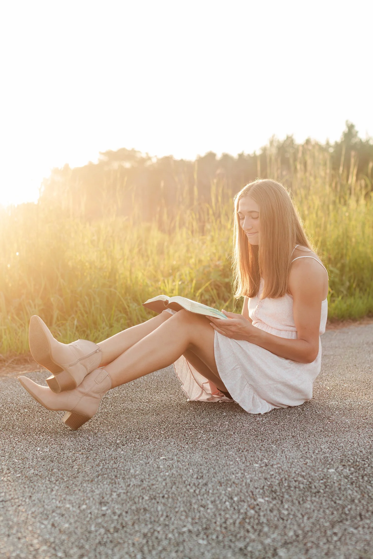 Young woman seated on a quiet road with sunlight behind her.