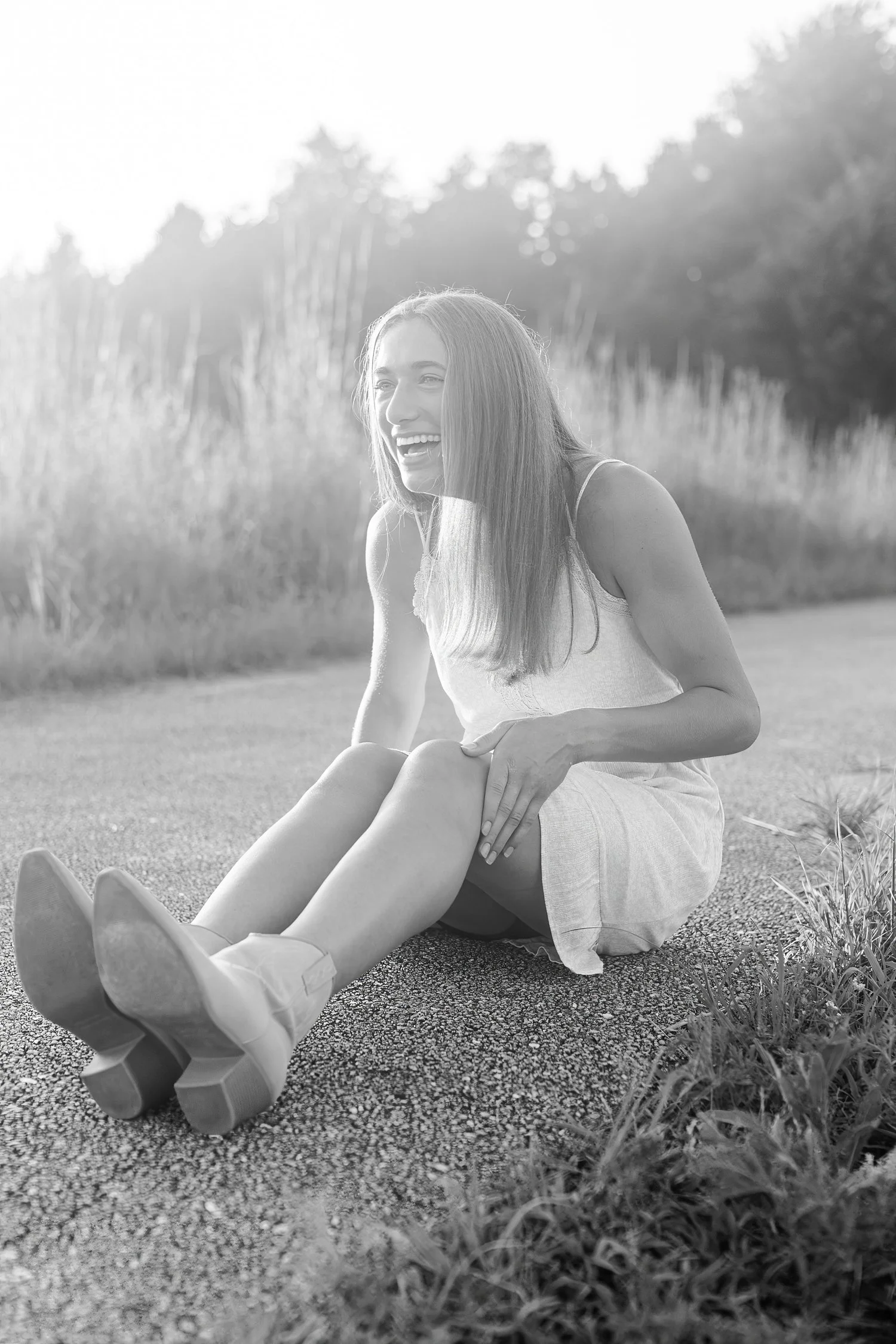 Black-and-white portrait of a young woman seated beside tall grass.