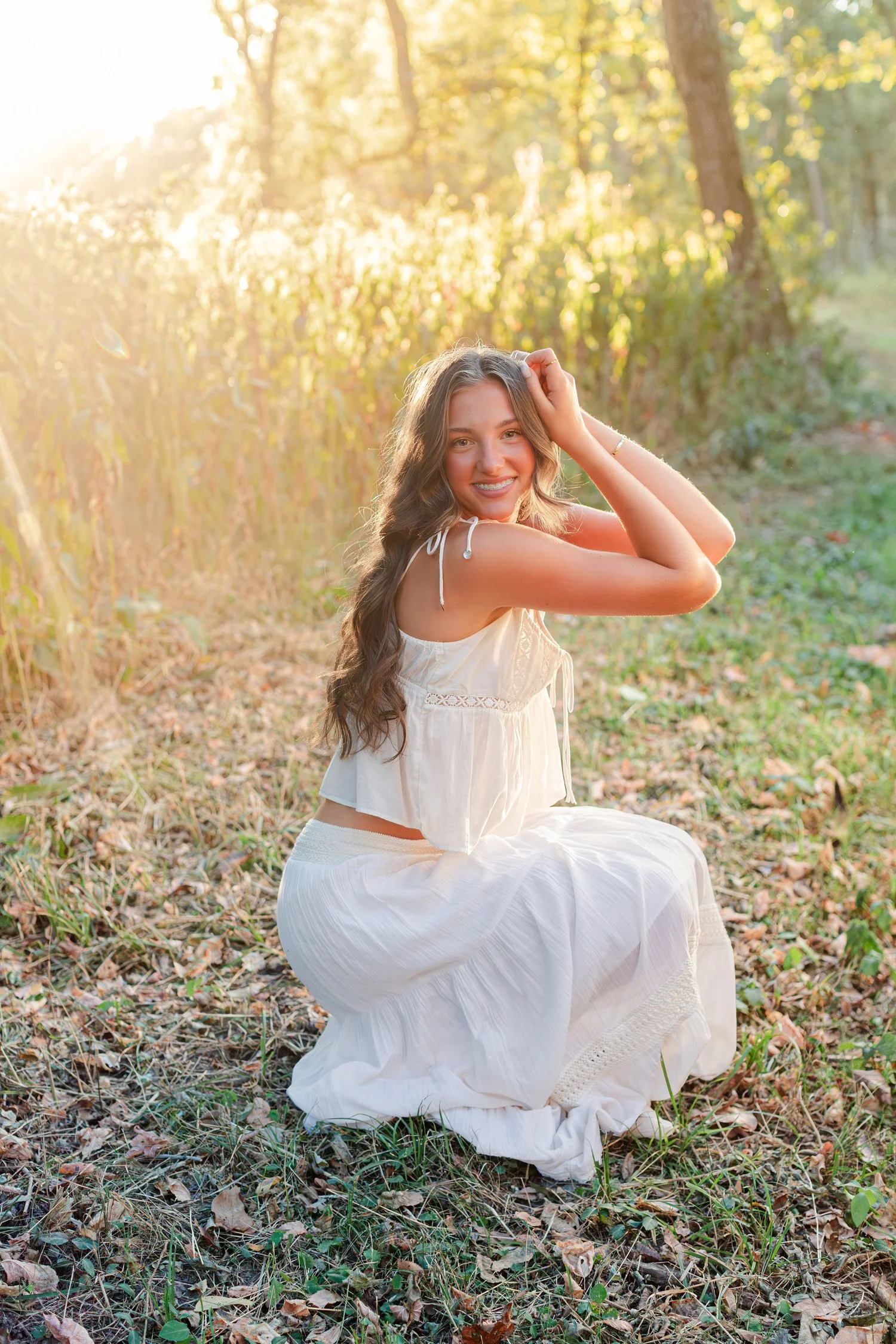 Eisley kneeling in golden grass in a white skirt, senior pictures near Bolivar, MO