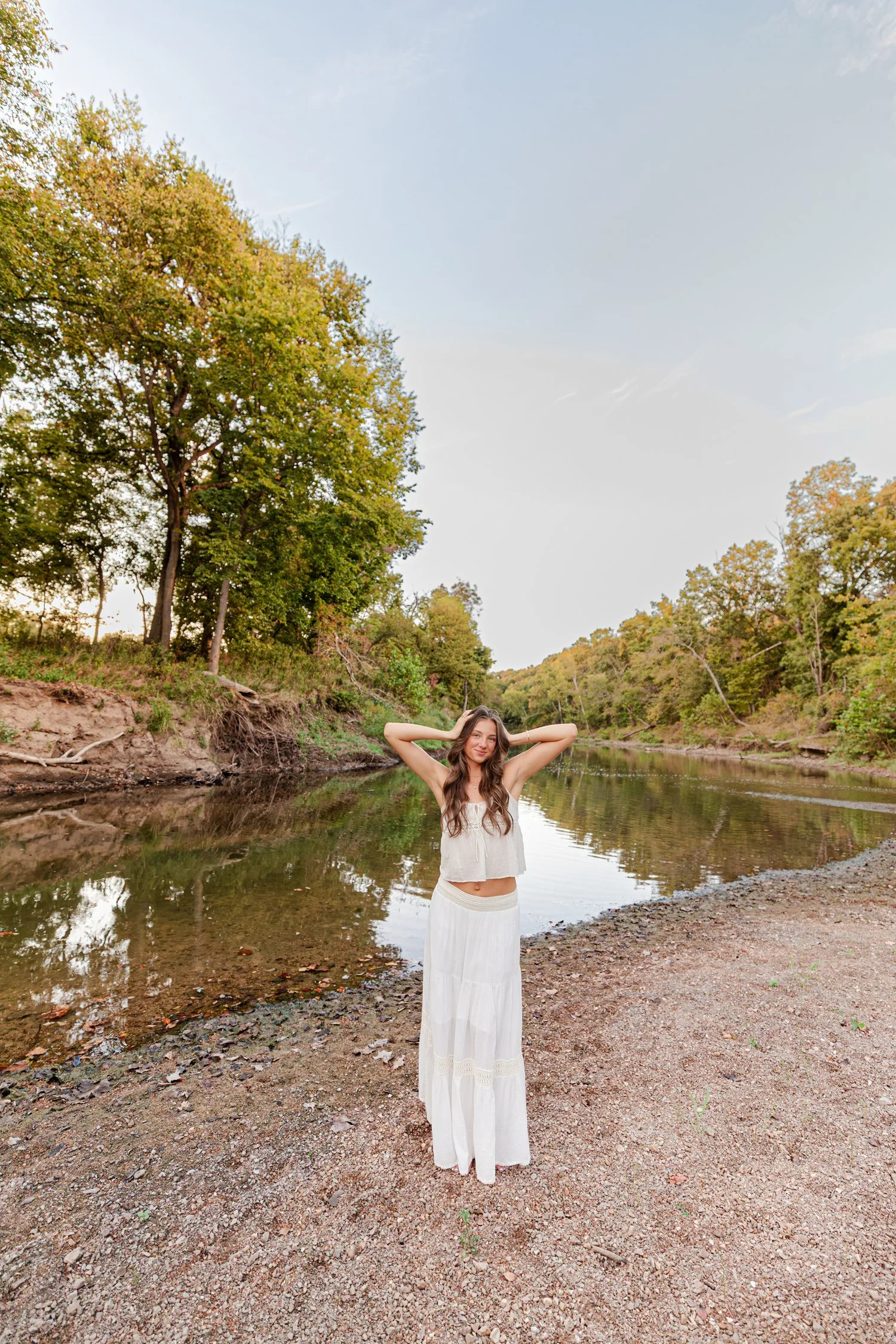 Eisley on the river gravel bar with her hands in her hair, senior pictures near Bolivar, MO