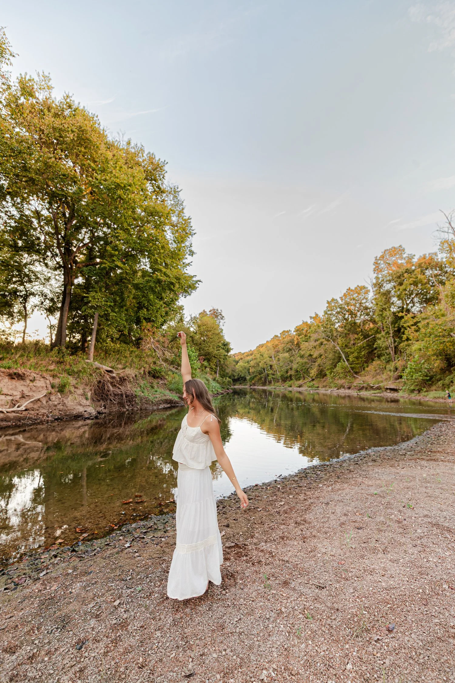 Eisley in a white skirt looking back on the riverbank, senior pictures near Bolivar, MO