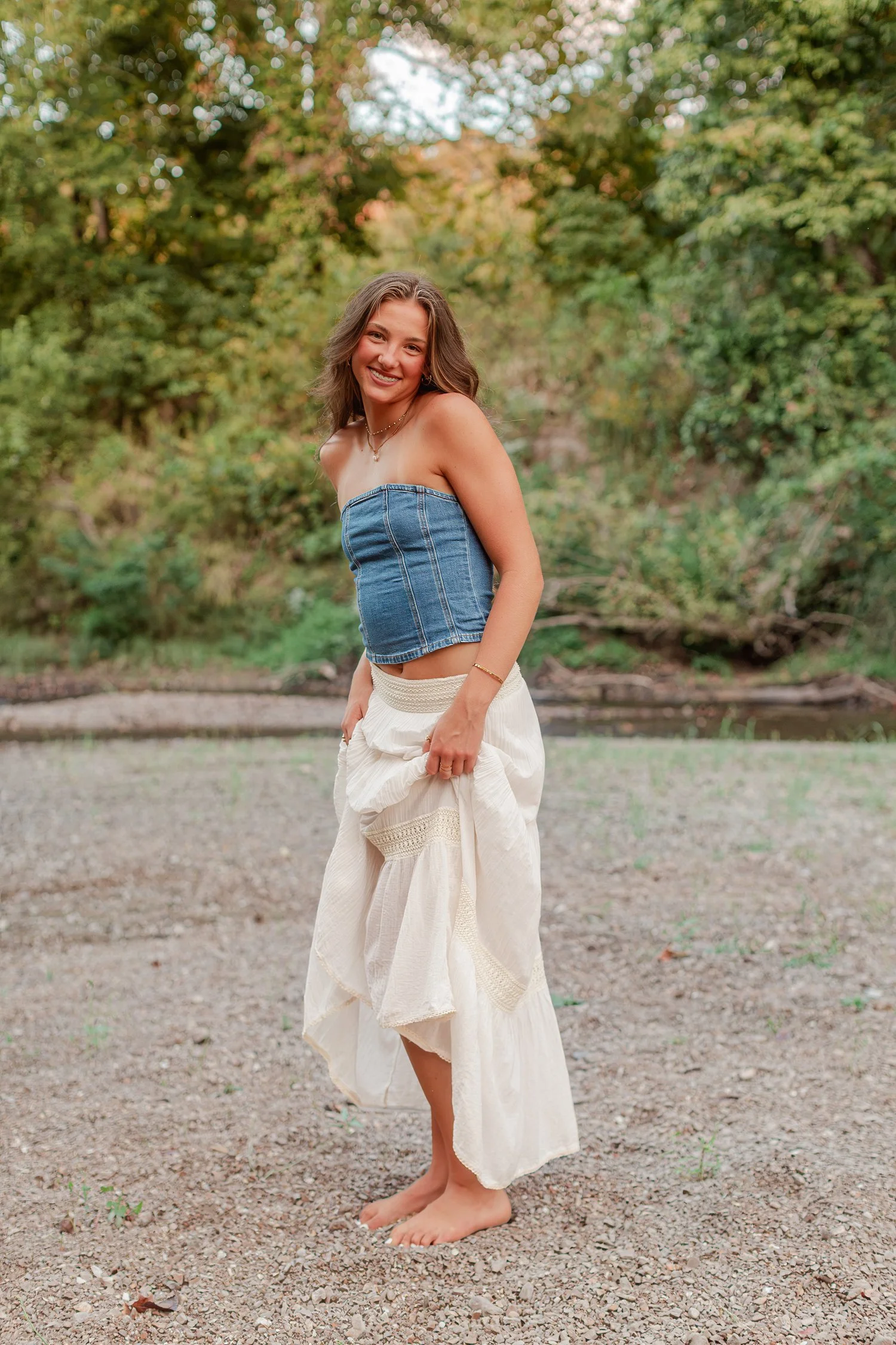 Eisley barefoot in a denim top holding her white skirt, senior pictures near Bolivar, MO