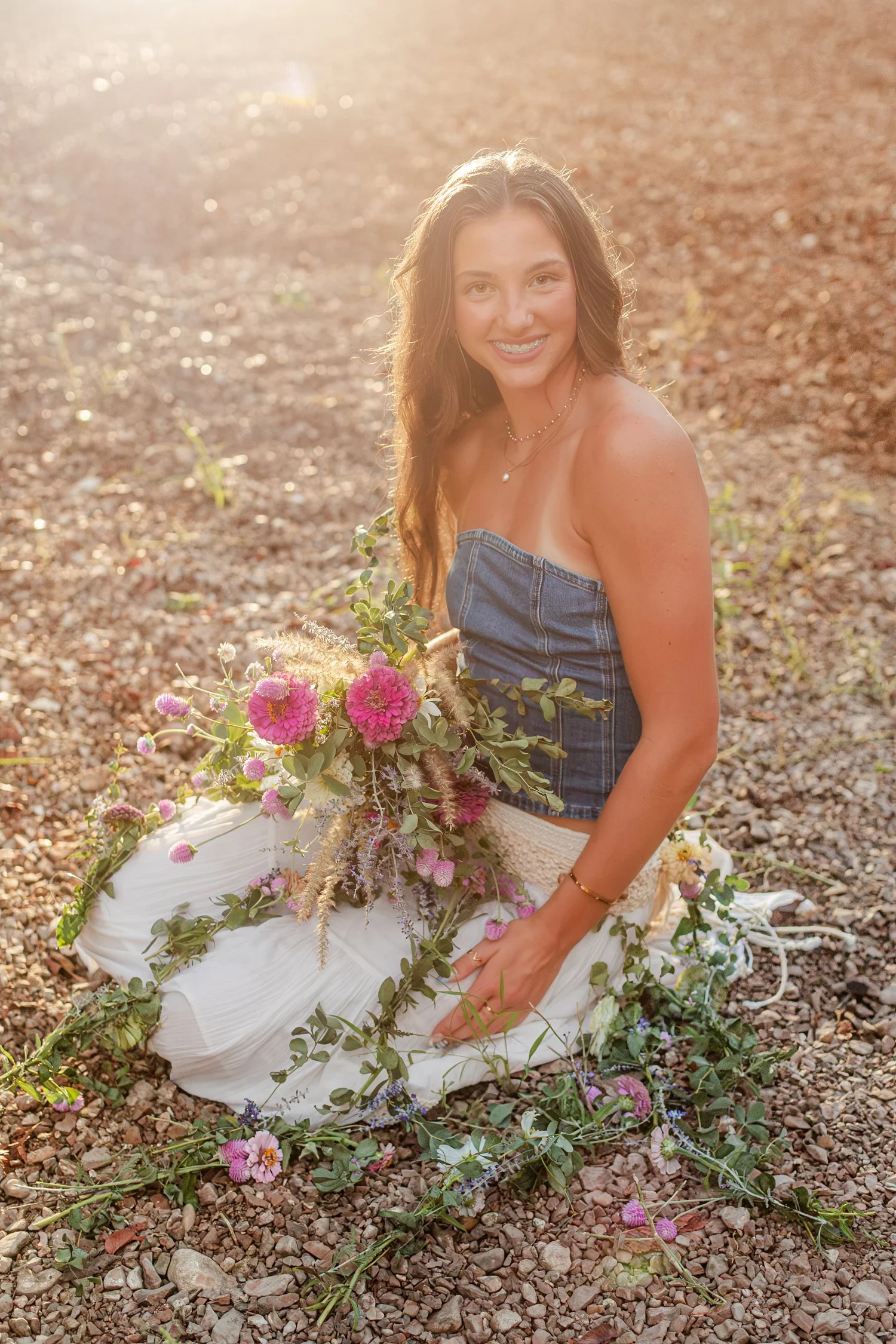 Eisley sitting on the gravel with her wildflower bouquet, senior session near Bolivar, MO
