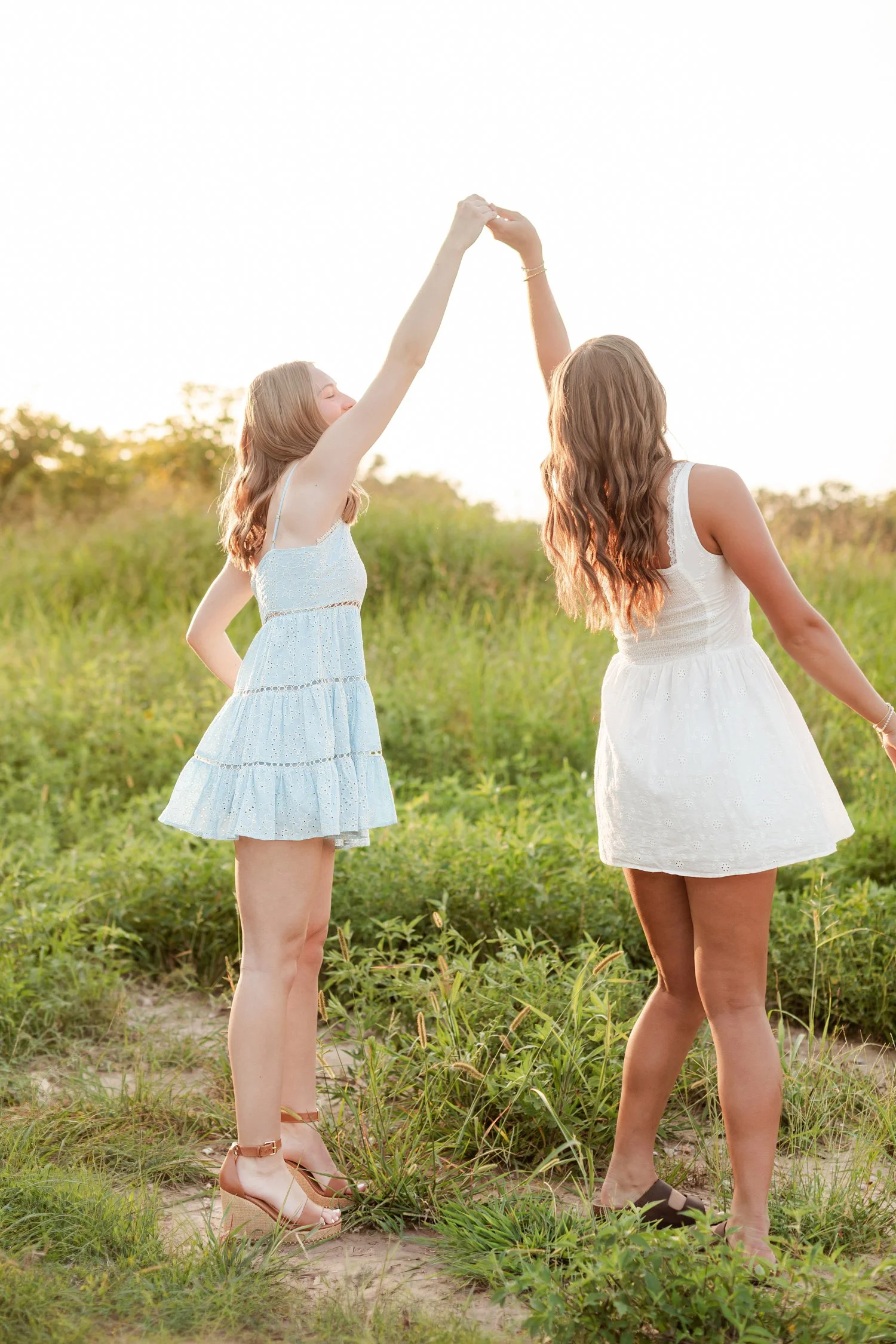 Two seniors seen from the side with hands joined high overhead in tall grass, bestie senior pictures in Bolivar, MO