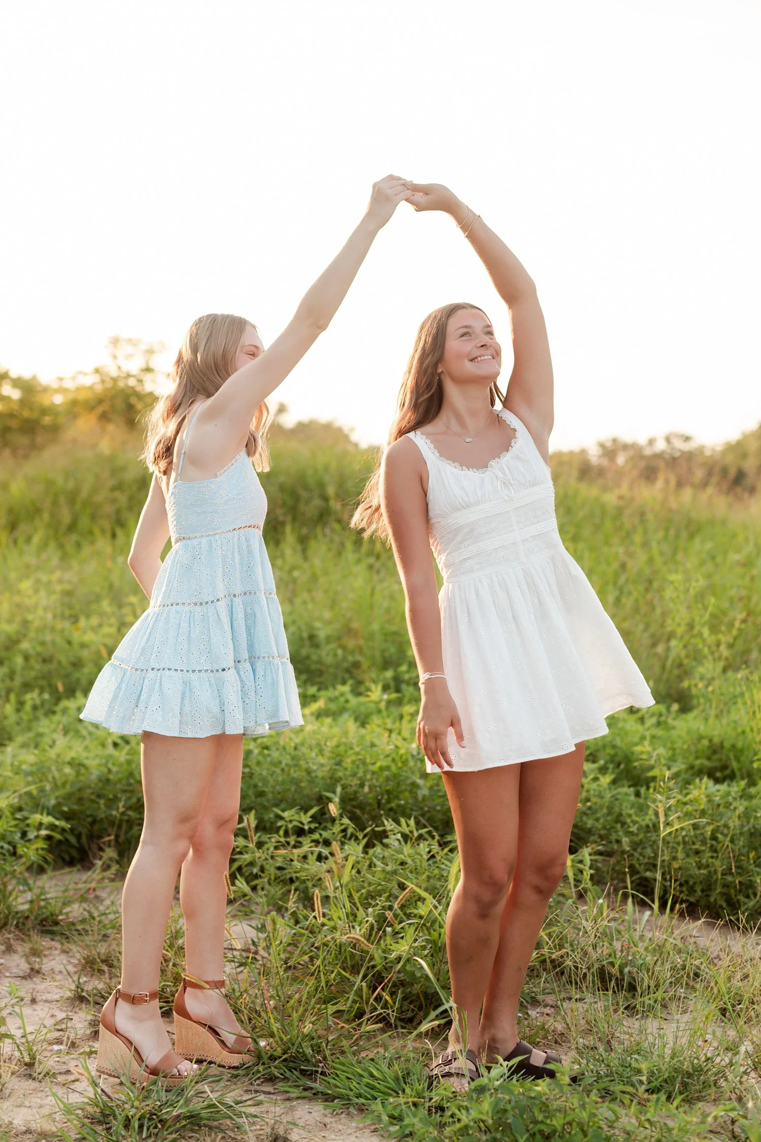 Two seniors facing forward under a raised hand arch in a green field, bestie senior pictures in Bolivar, MO