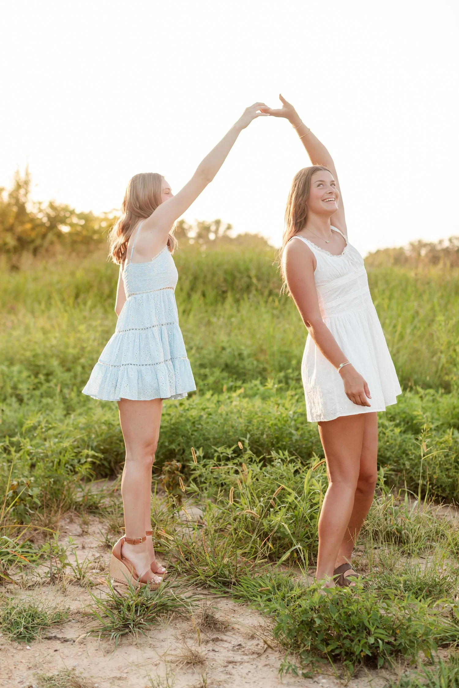 Senior in a light blue dress on tiptoe spinning a friend in a white dress, bestie senior pictures in Bolivar, MO