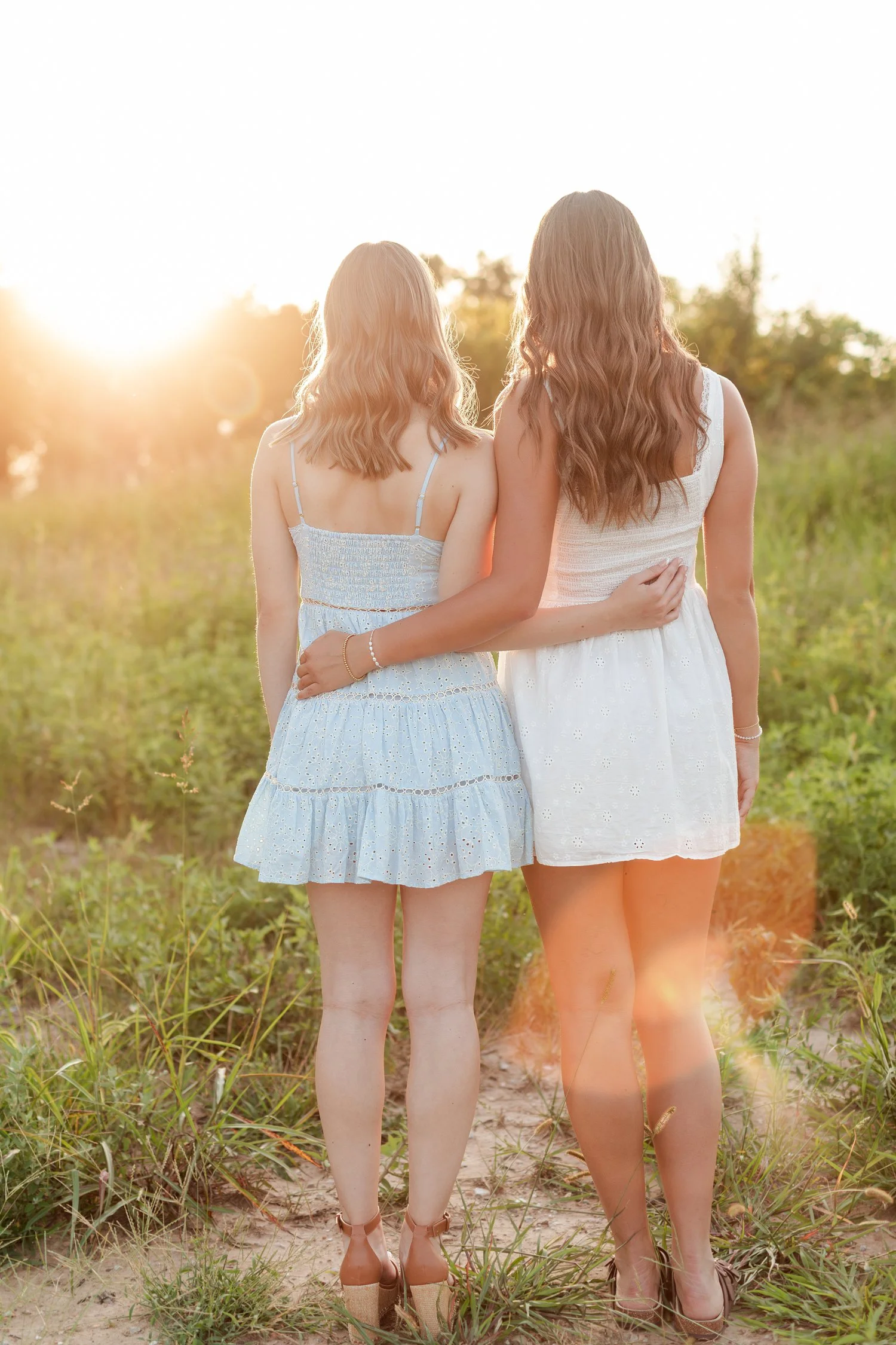 Two seniors seen from behind with arms around each other facing the setting sun, bestie senior pictures in Bolivar, MO