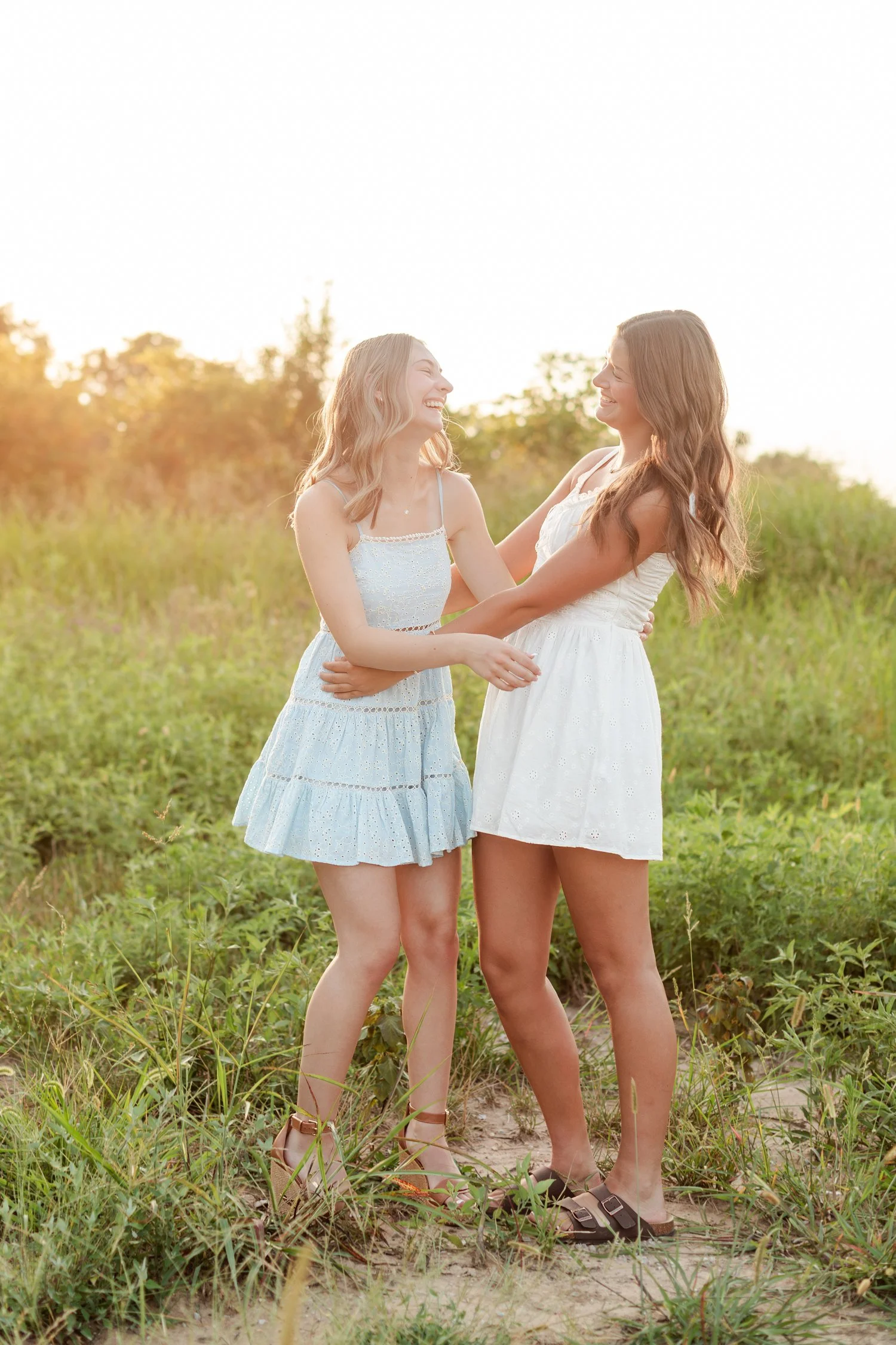 Two seniors in sundresses laughing while holding each other in a green field, bestie senior pictures in Bolivar, MO