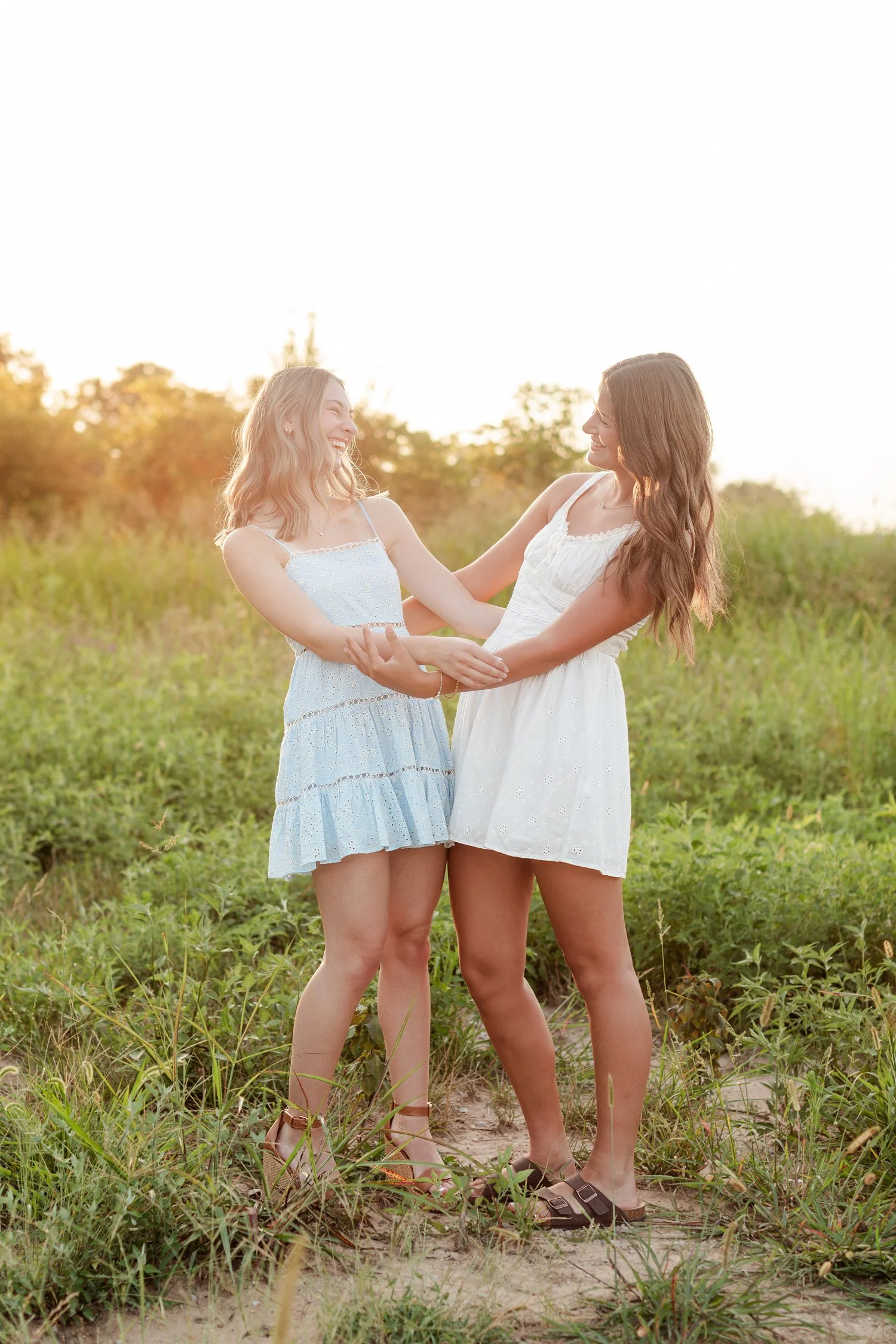 Two seniors in sundresses holding both hands and smiling at each other, bestie senior pictures in Bolivar, MO