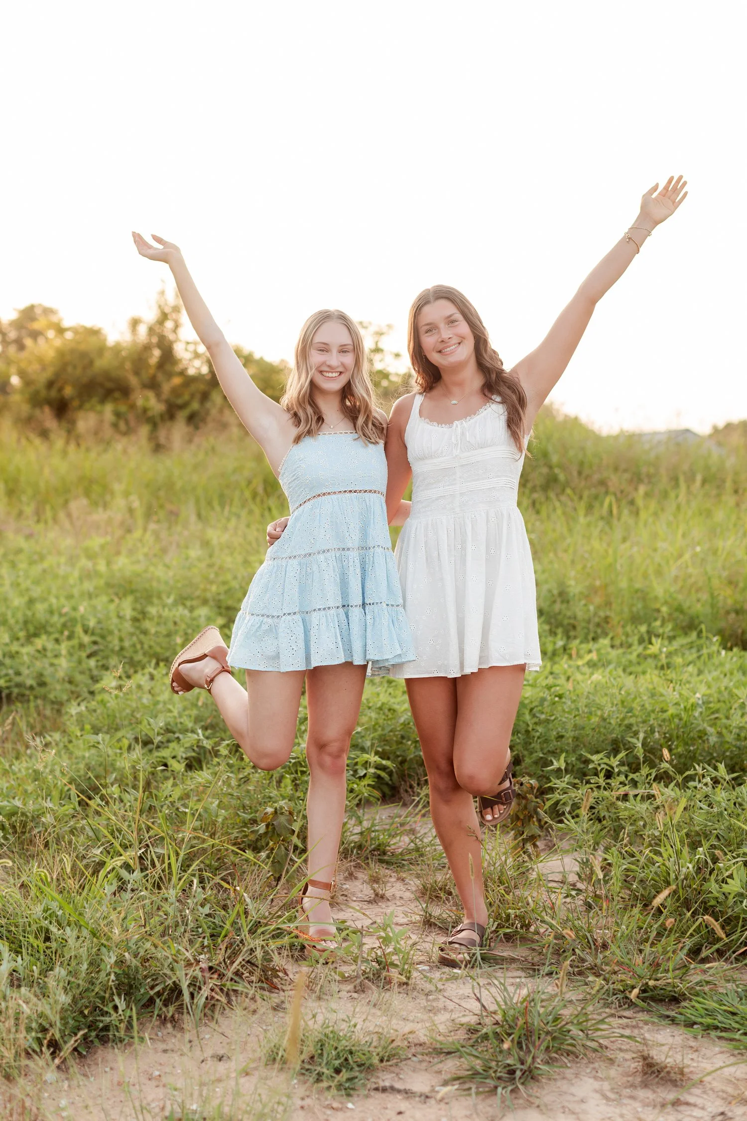 Two seniors with arms raised high, each balancing on one foot in the field, bestie senior pictures in Bolivar, MO