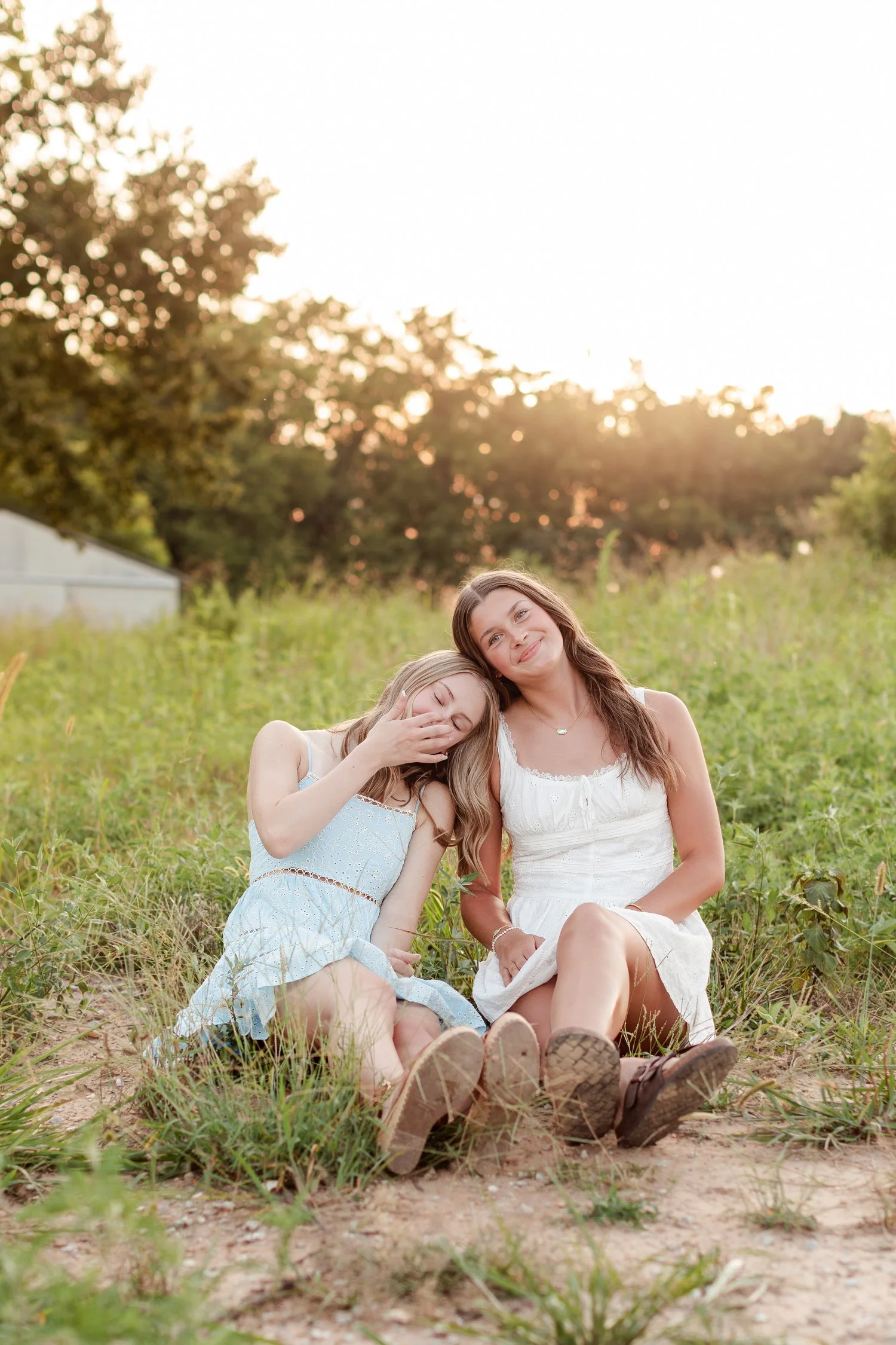 Two seniors sitting in the grass, one resting against the other's shoulder with eyes closed, bestie senior pictures in Bolivar, MO