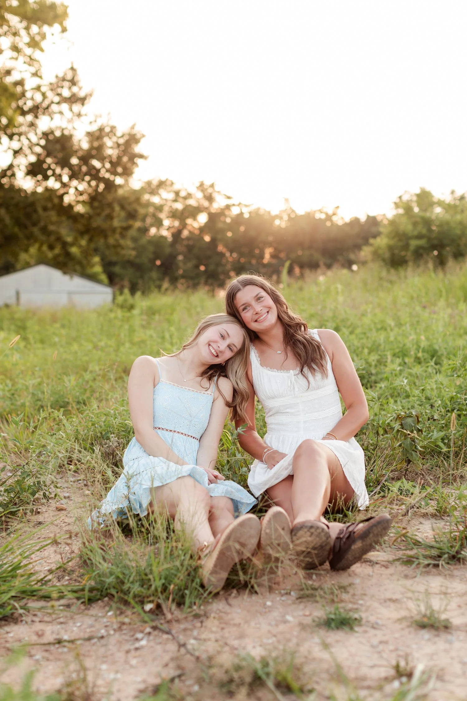 Two seniors sitting close together on a dirt patch in the field with heads tilted together, bestie senior pictures in Bolivar, MO