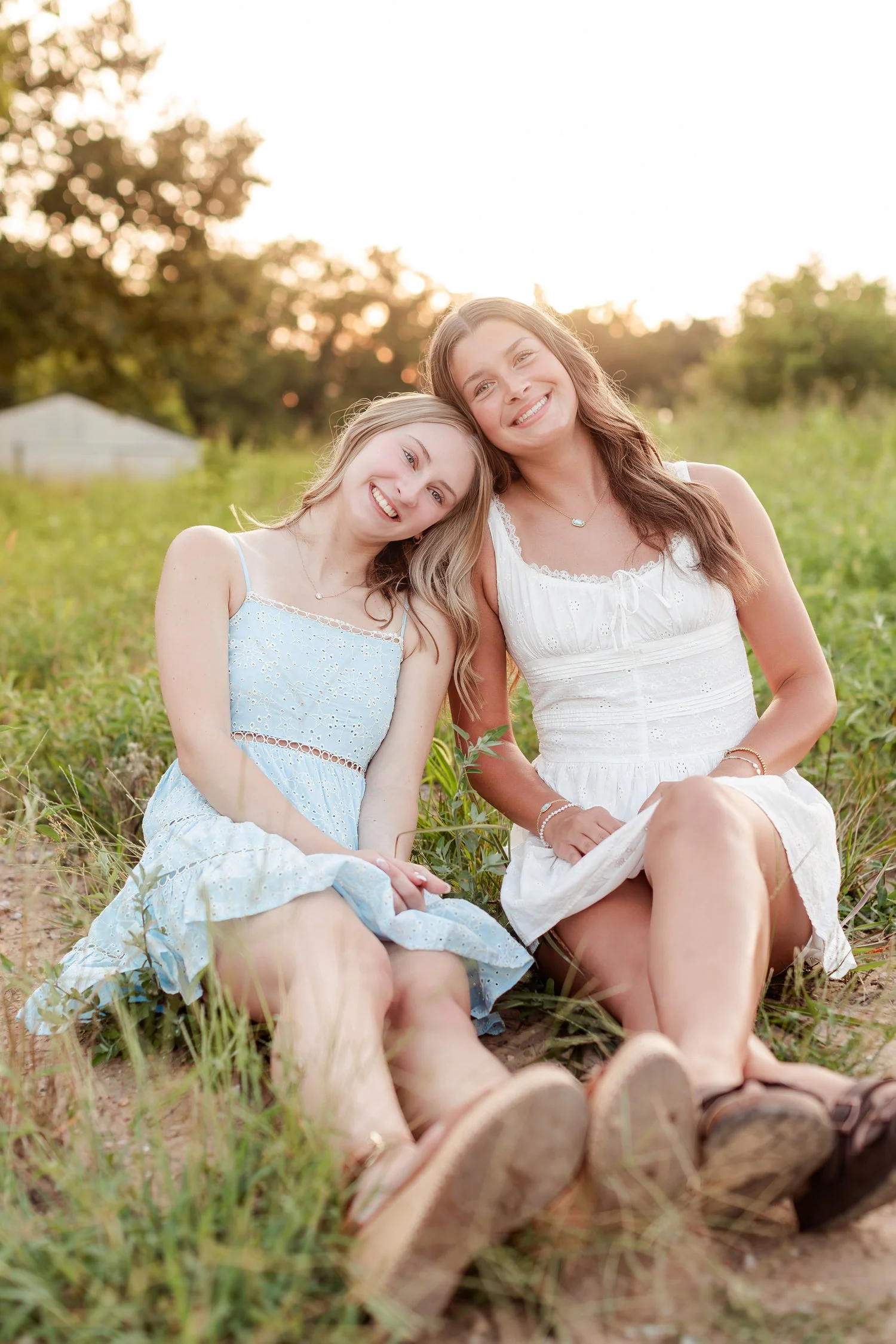 Close view of two seniors sitting in the grass with heads leaned together, smiling, bestie senior pictures in Bolivar, MO