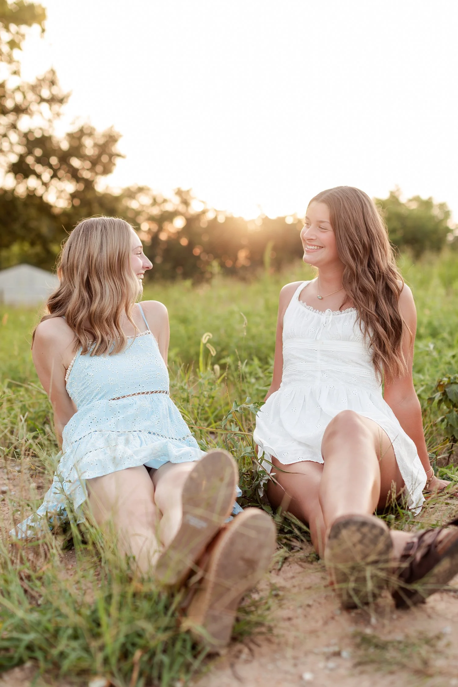 Two seniors sitting in the grass laughing at each other with boots in the foreground, bestie senior pictures in Bolivar, MO