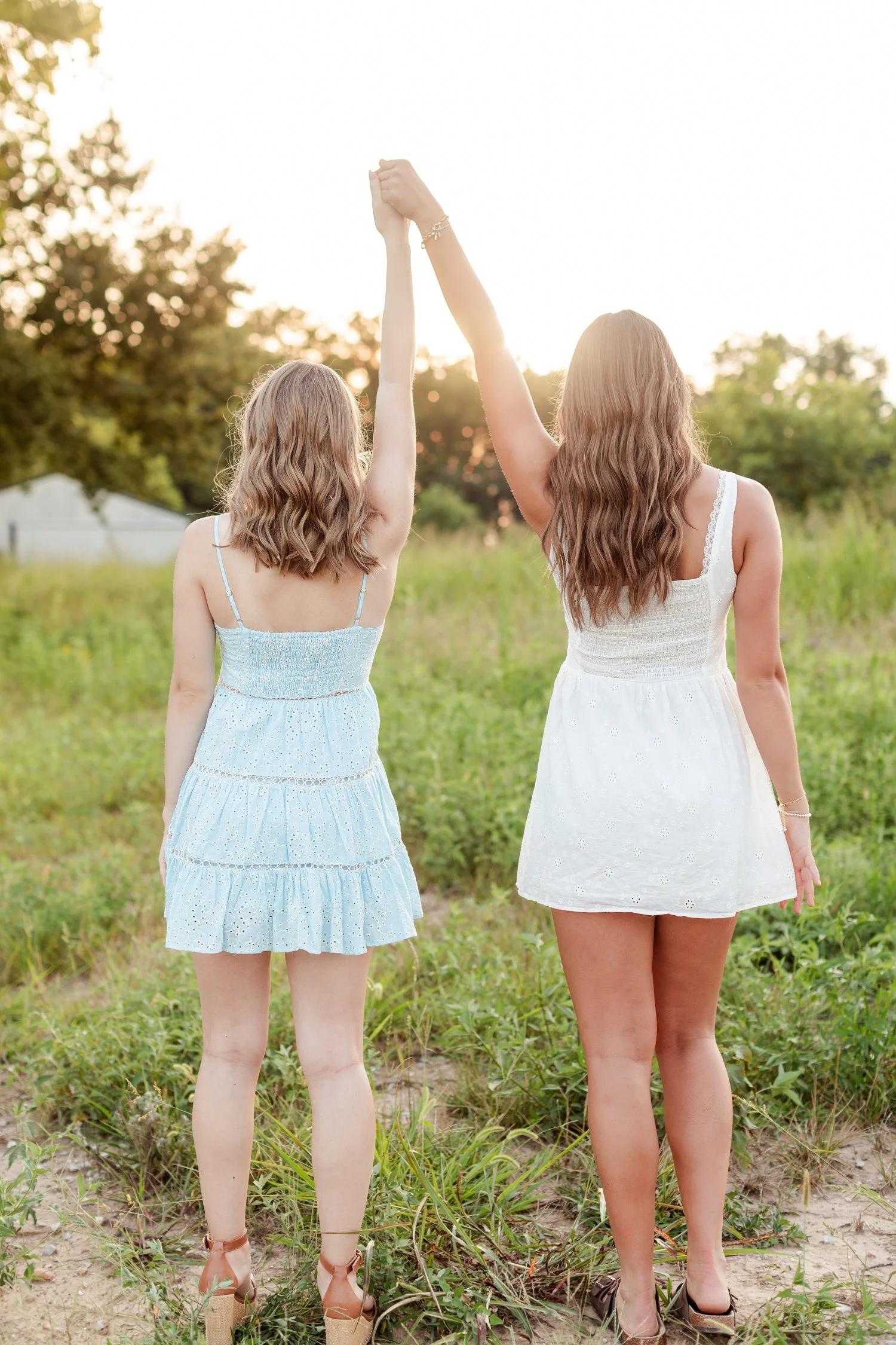 Two seniors seen from behind holding joined hands high over the field, bestie senior pictures in Bolivar, MO