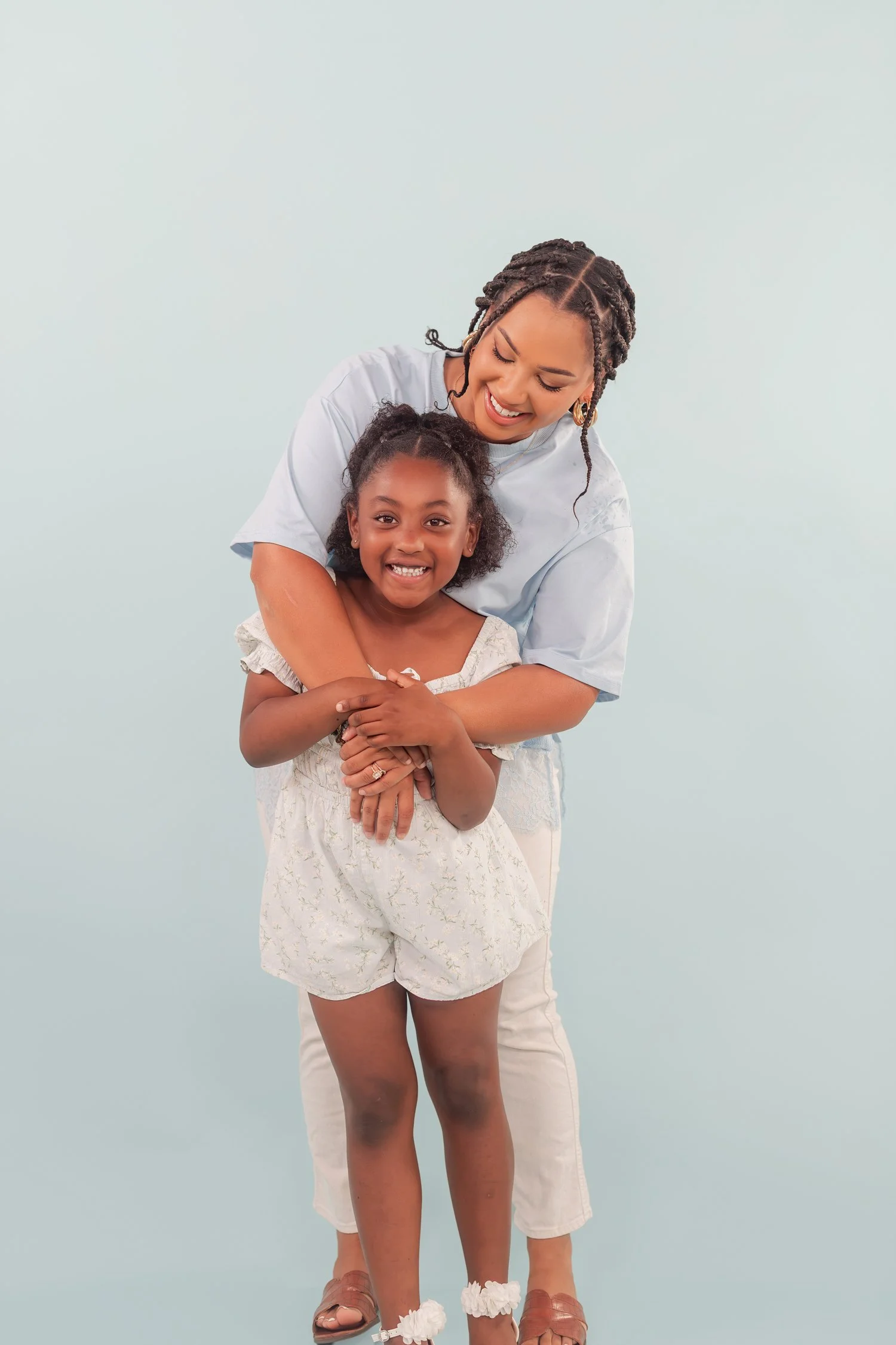 Mother leaning over a daughter in a white romper, both smiling at the camera in the studio, mother daughter photos in Bolivar, MO