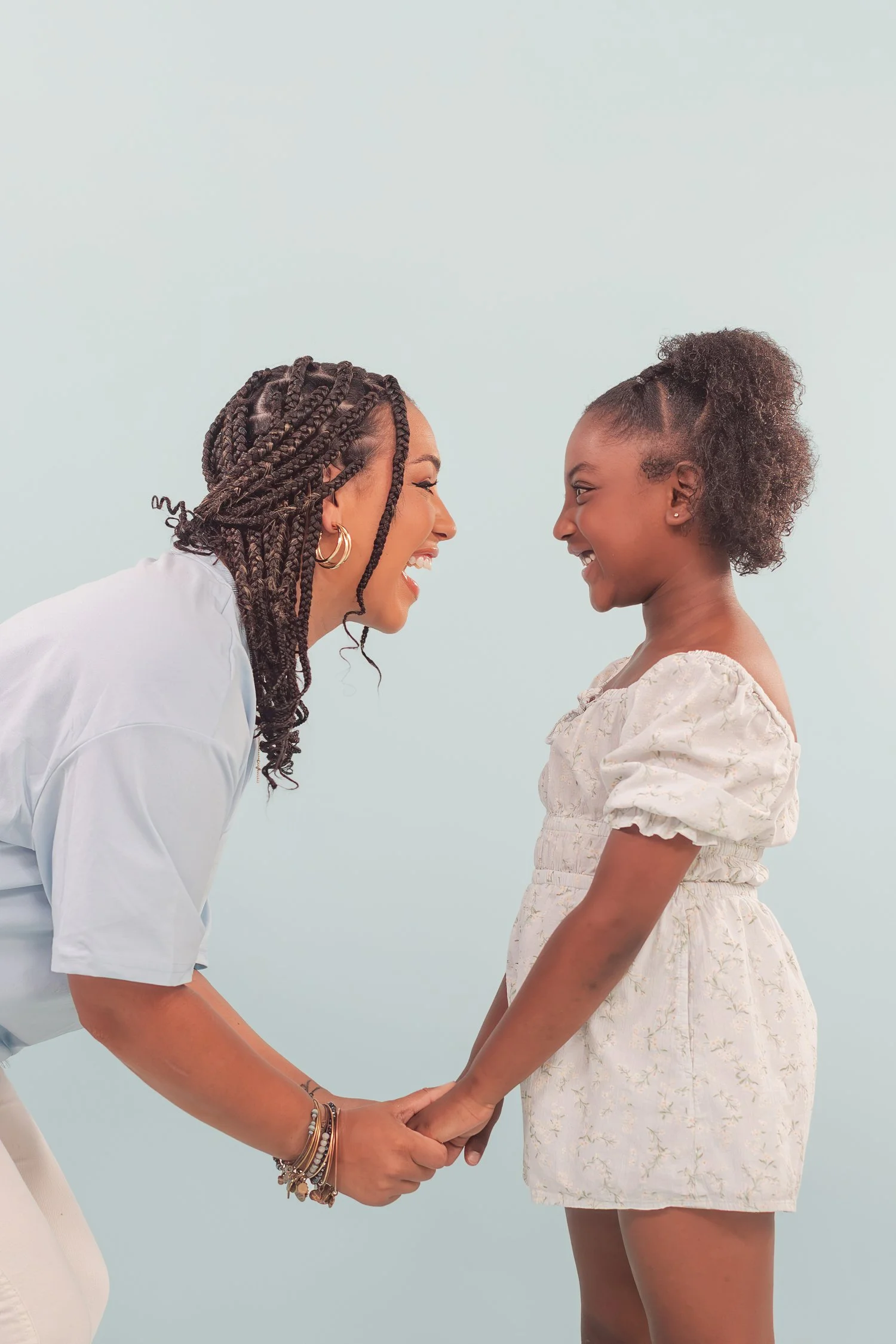 Mother and daughter holding hands and leaning in nose to nose against a pale blue backdrop, mother daughter photos in Bolivar, MO