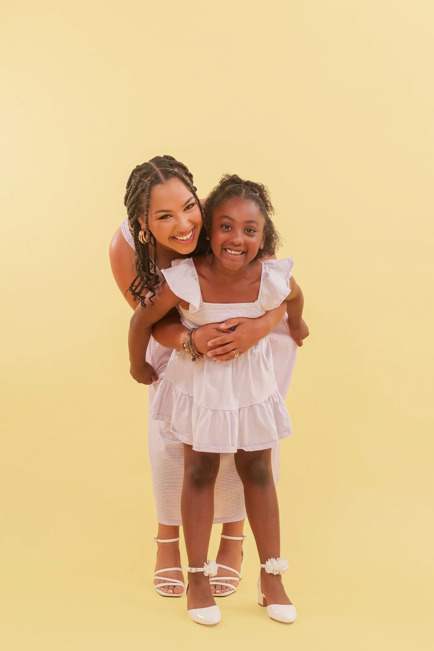 Mother hugging a daughter in a lavender dress from behind against a yellow backdrop, mother daughter photos in Bolivar, MO