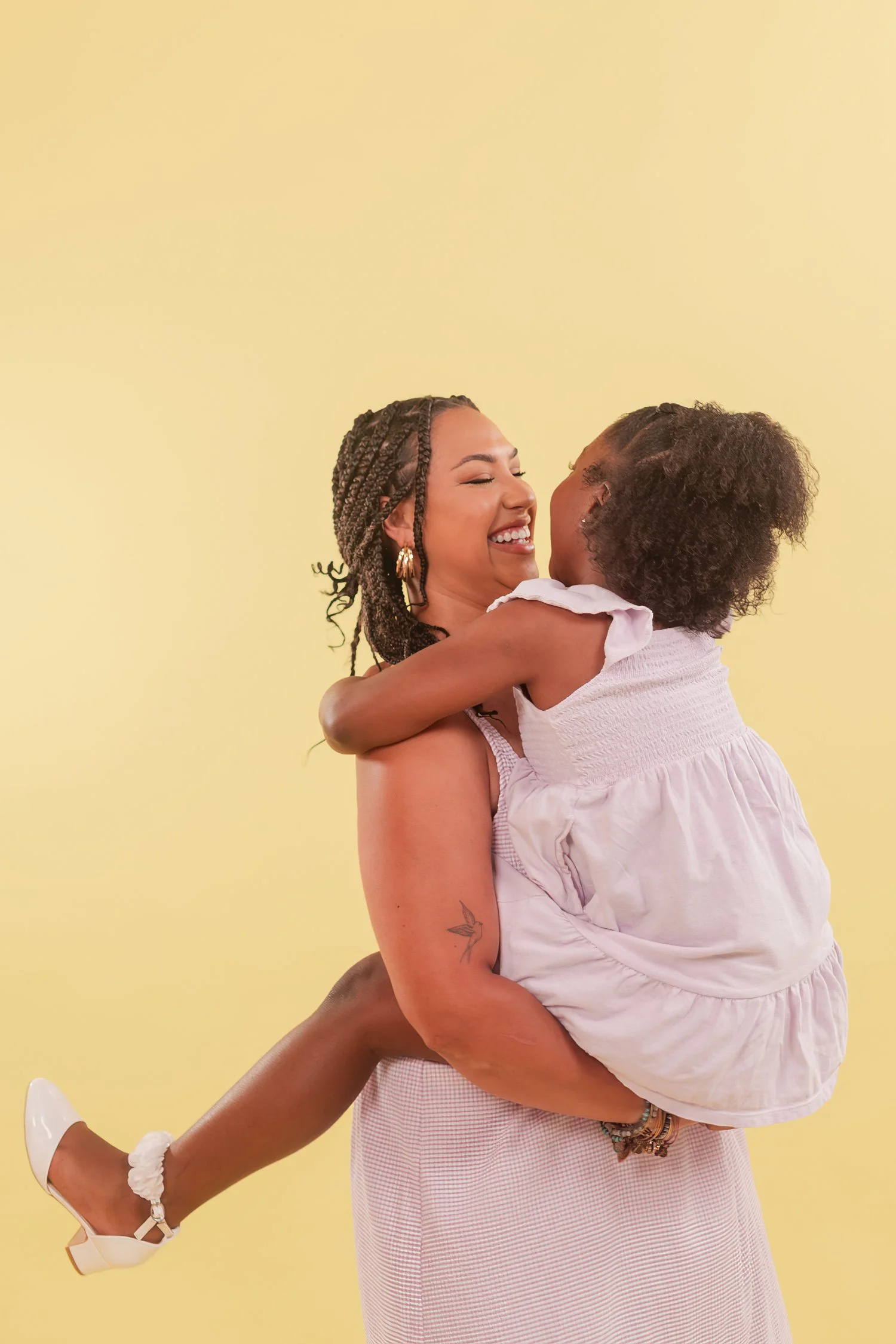 Mother lifting a daughter in a lavender dress onto one hip against a yellow backdrop, mother daughter photos in Bolivar, MO