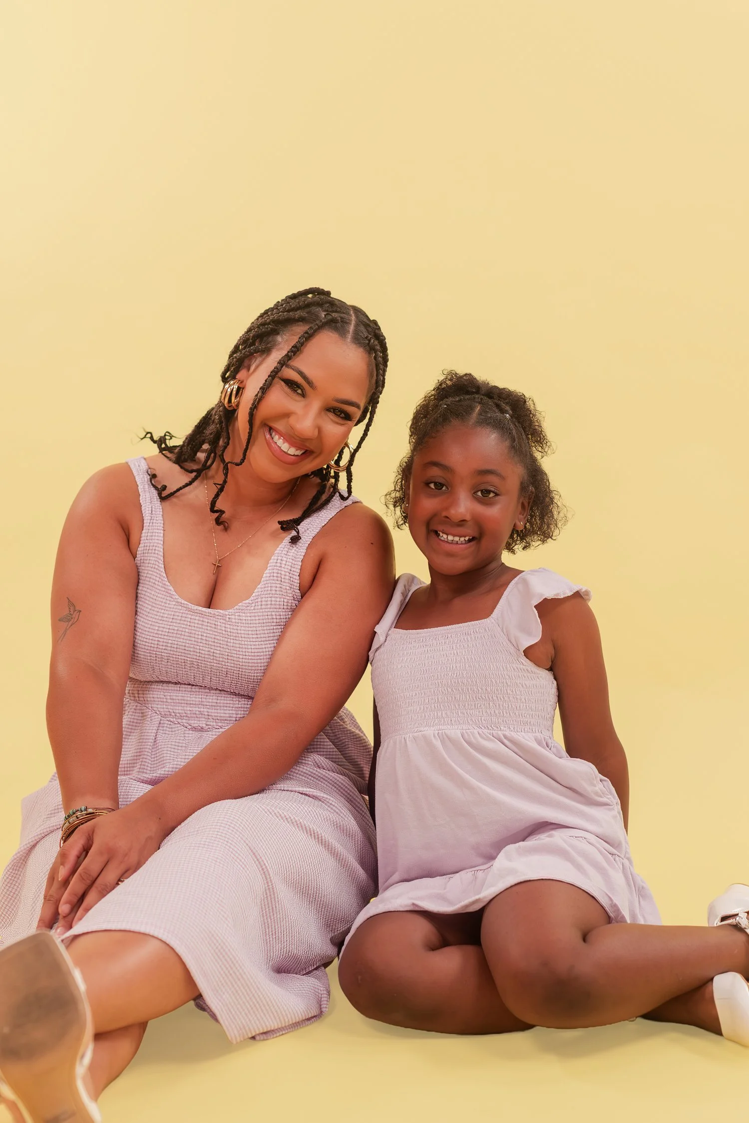 Mother and daughter in lavender dresses sitting side by side on a yellow studio floor, mother daughter photos in Bolivar, MO