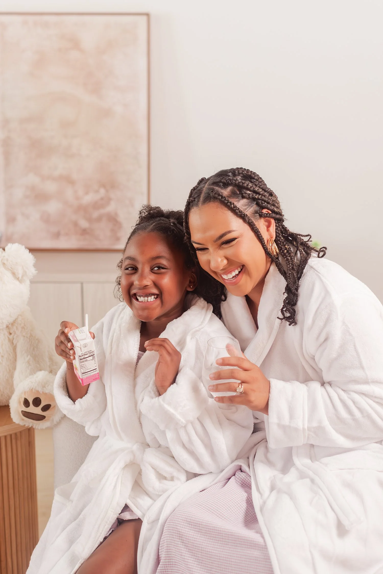 Mother and daughter in white robes laughing and holding drinks on a studio couch, mother daughter photos in Bolivar, MO