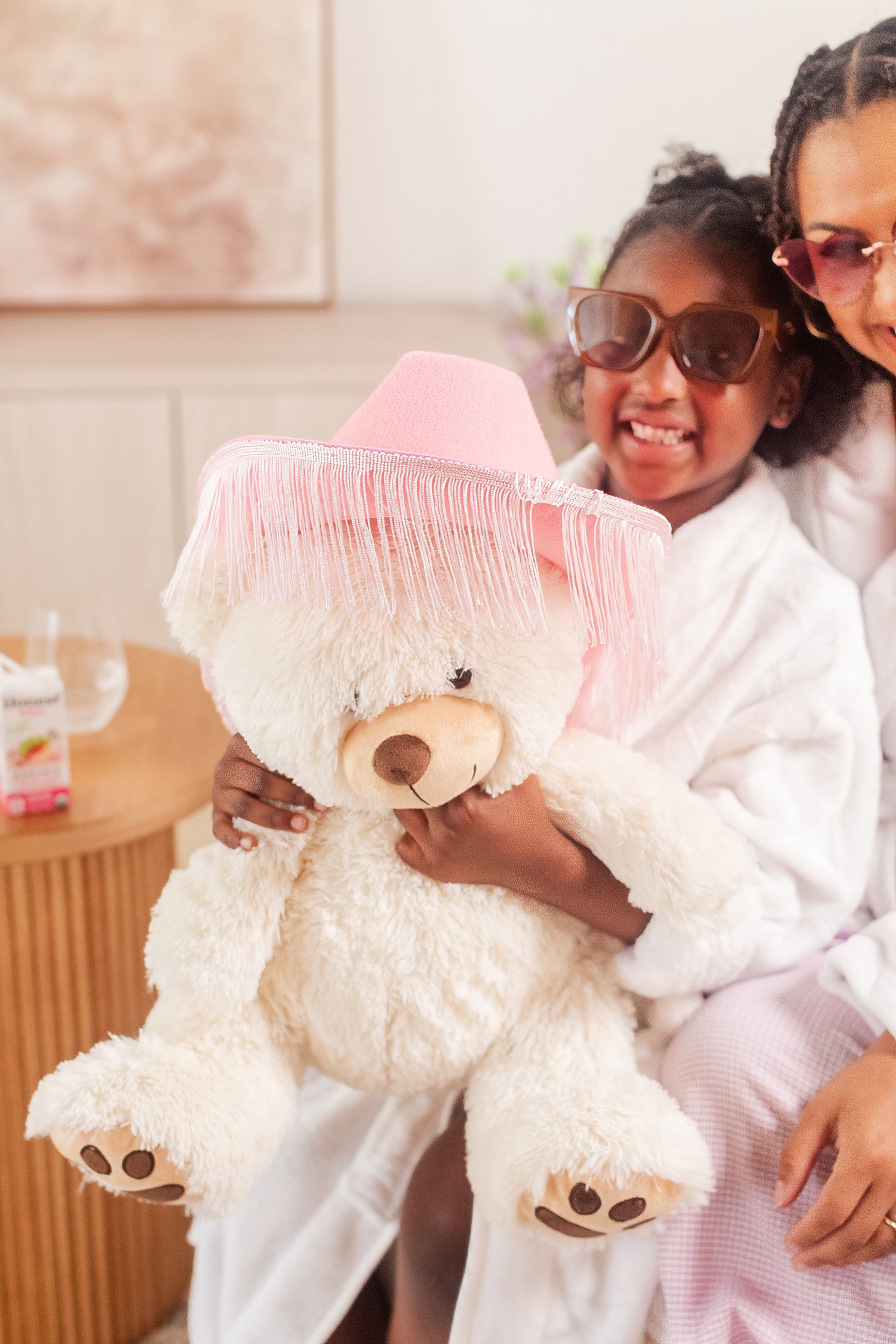 Daughter in sunglasses hugging a teddy bear that wears a pink fringed cowboy hat, mother daughter photos in Bolivar, MO