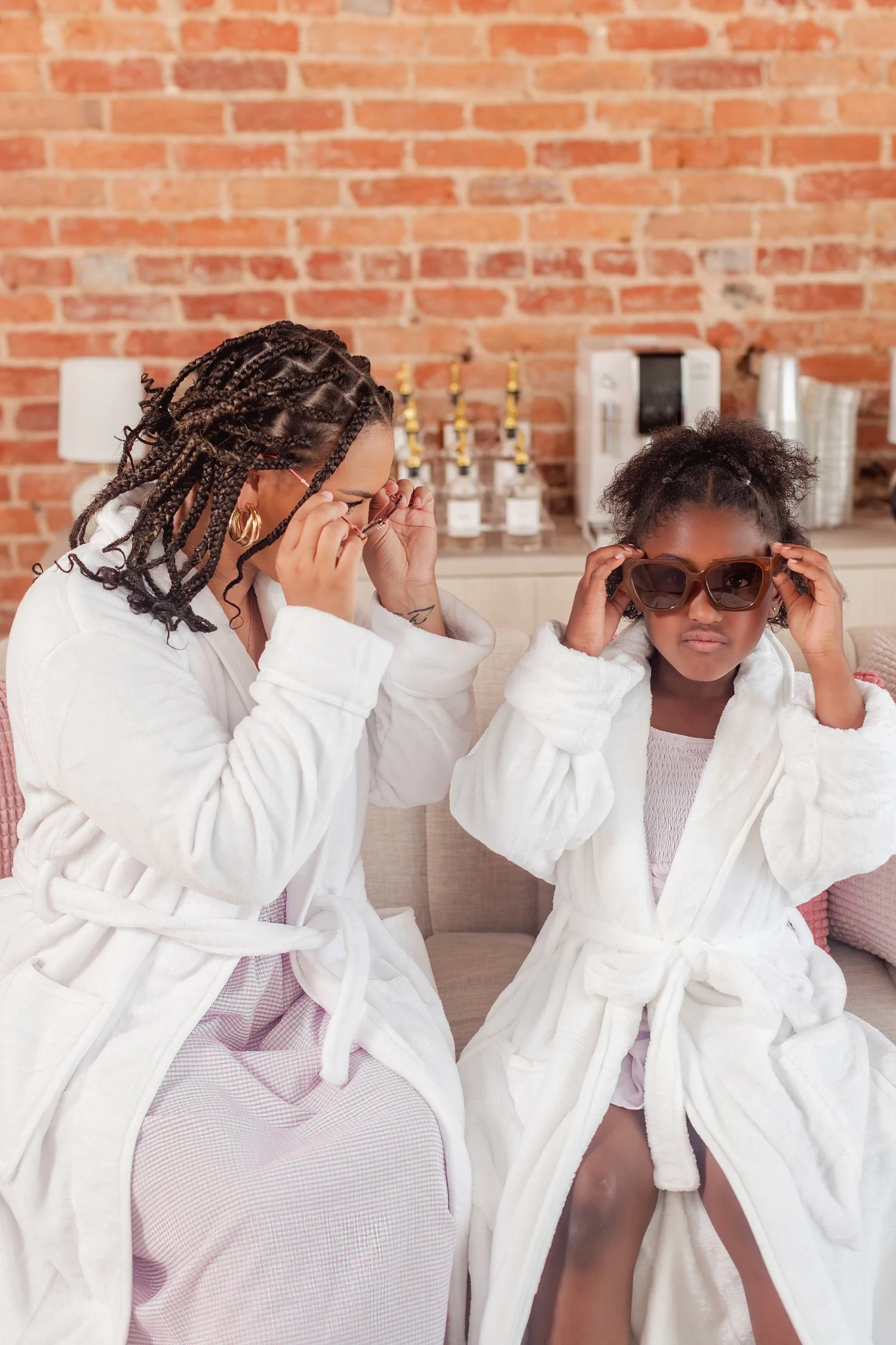 Mother and daughter in white robes lowering sunglasses in front of a brick wall, mother daughter photos in Bolivar, MO
