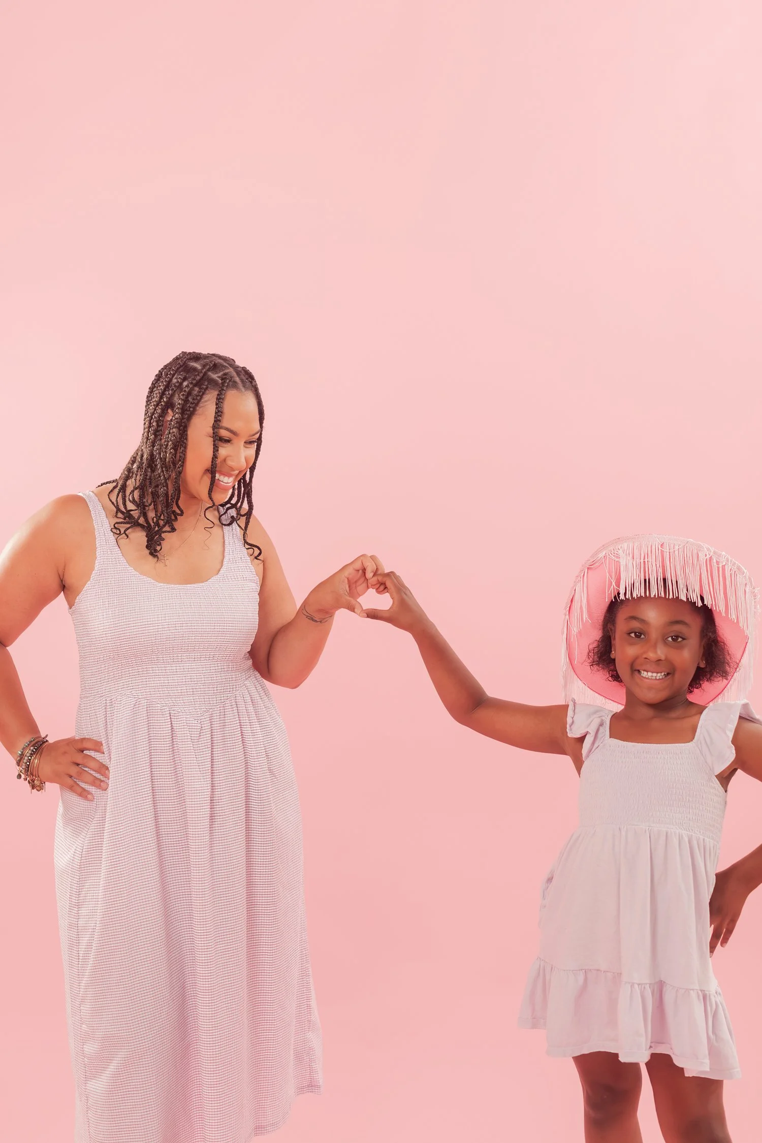 Mother and daughter in lavender dresses doing a fist bump against a pink backdrop, mother daughter photos in Bolivar, MO