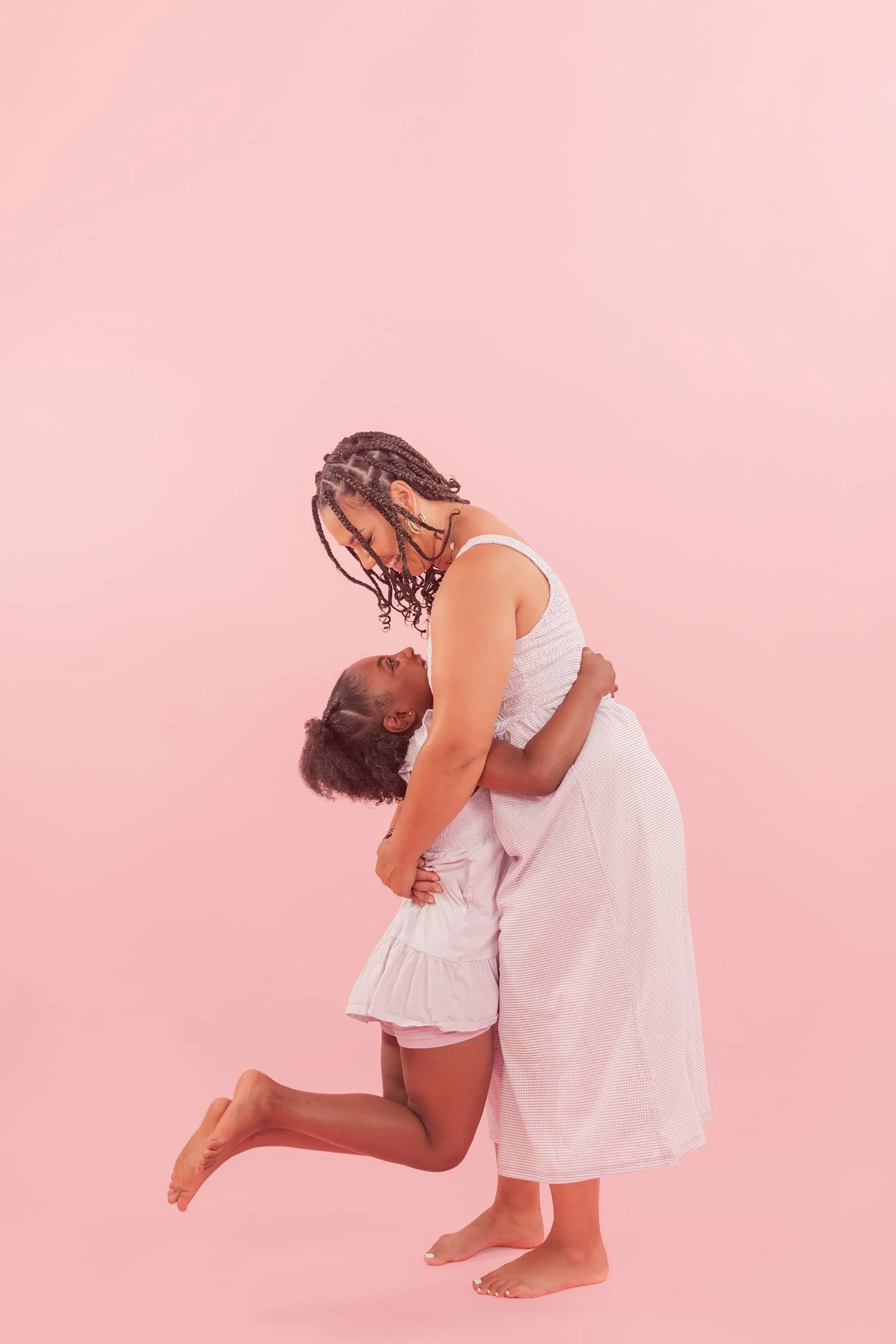 Daughter jumping into mother's arms for a hug against a pink backdrop, mother daughter photos in Bolivar, MO