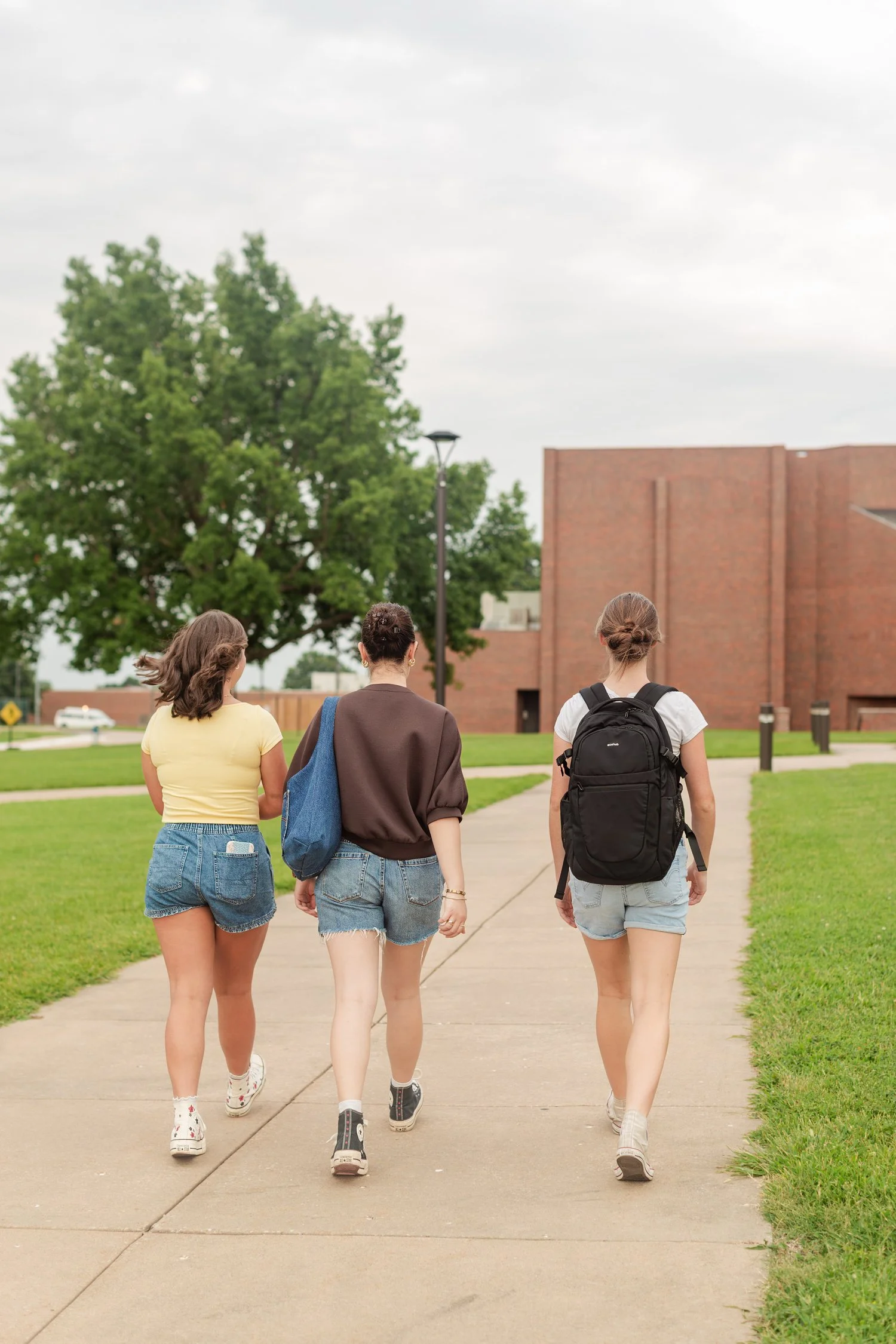 Three friends with backpacks walking along a campus path.