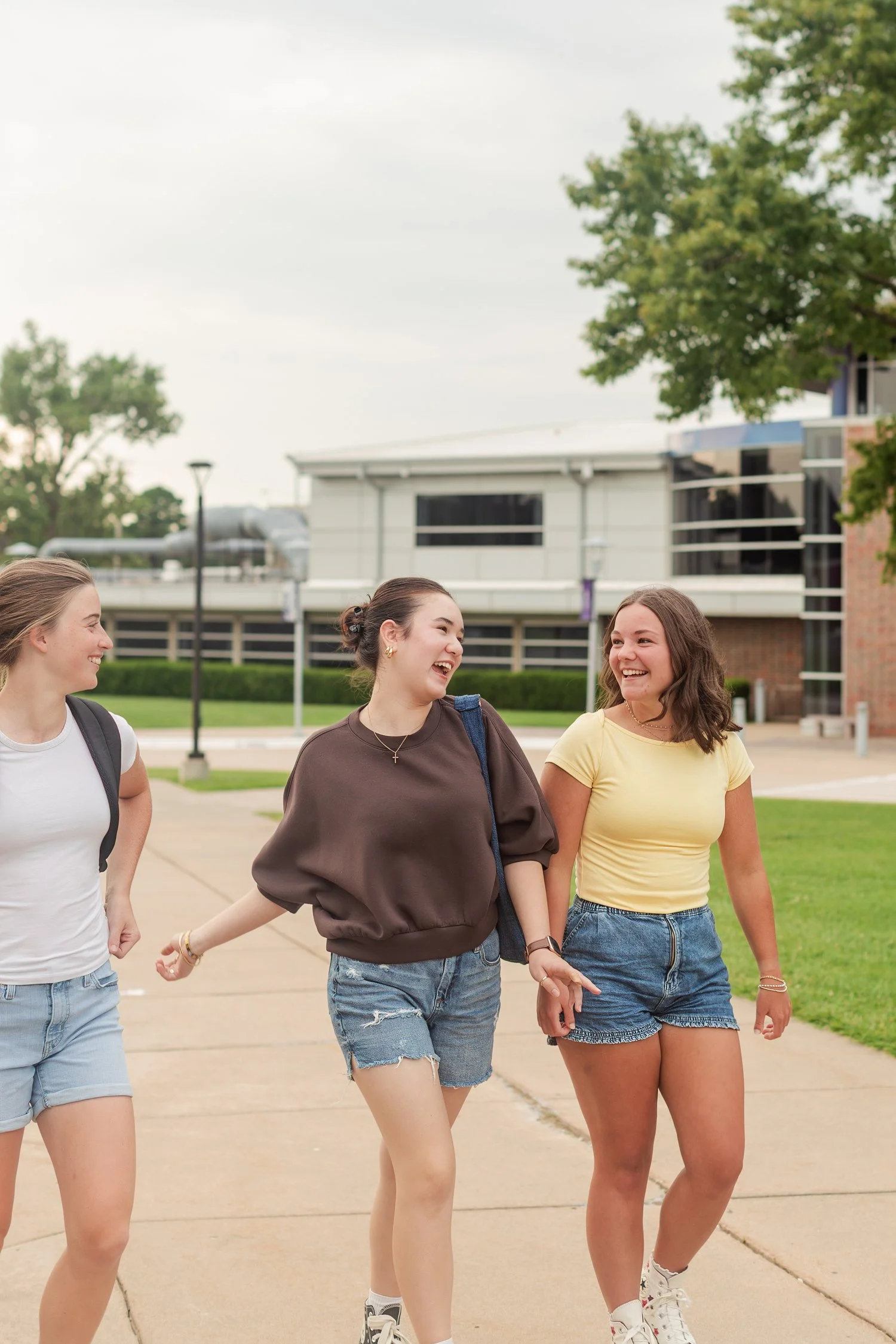 Three friends talking and walking together outside brick campus buildings.