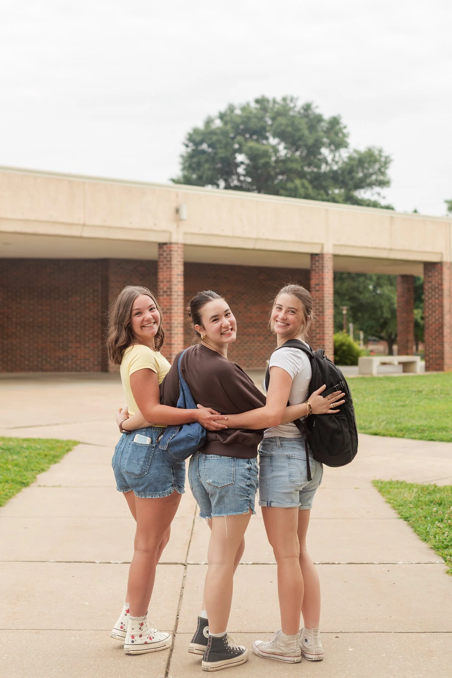 Three friends standing close together on a campus walkway.