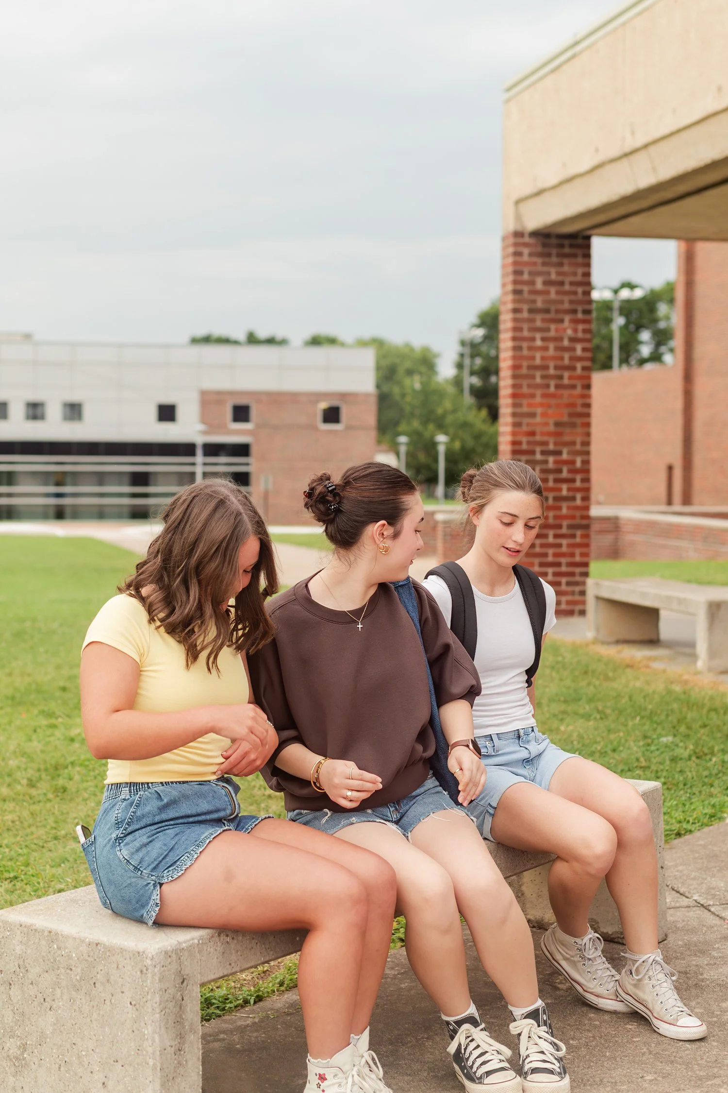 Three friends seated together on a stone bench outdoors.