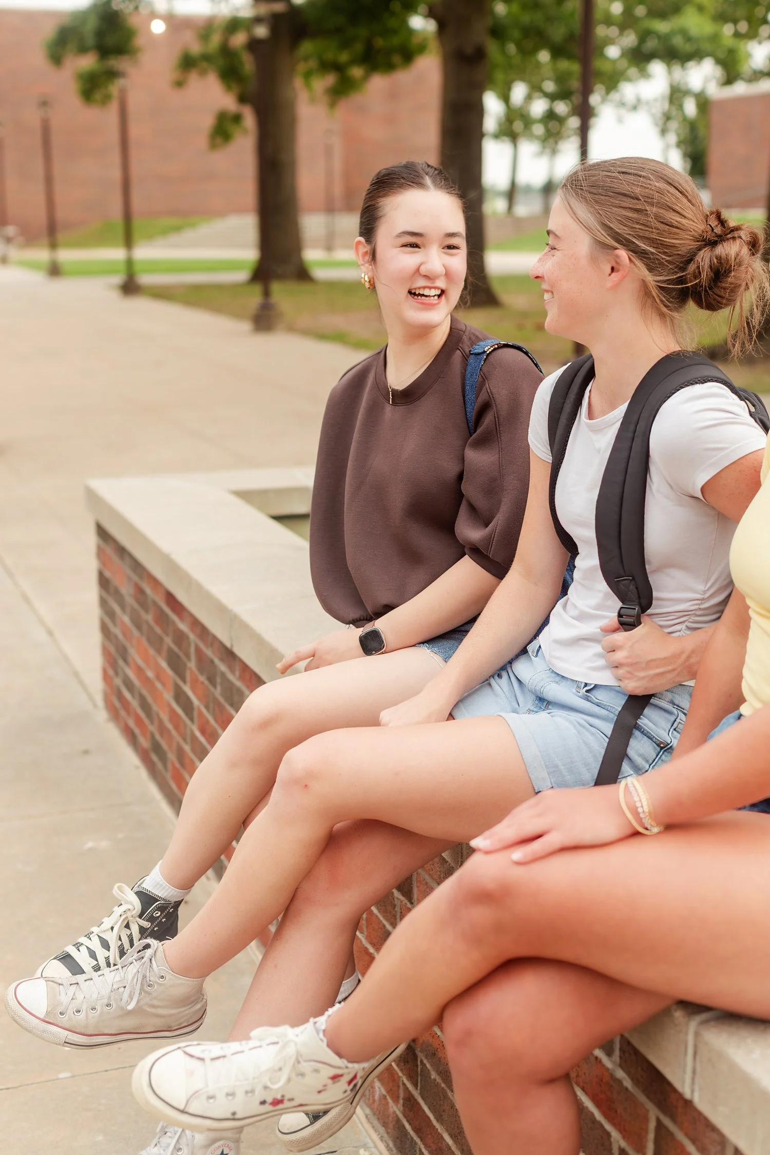Two friends laughing while seated together on a low wall.