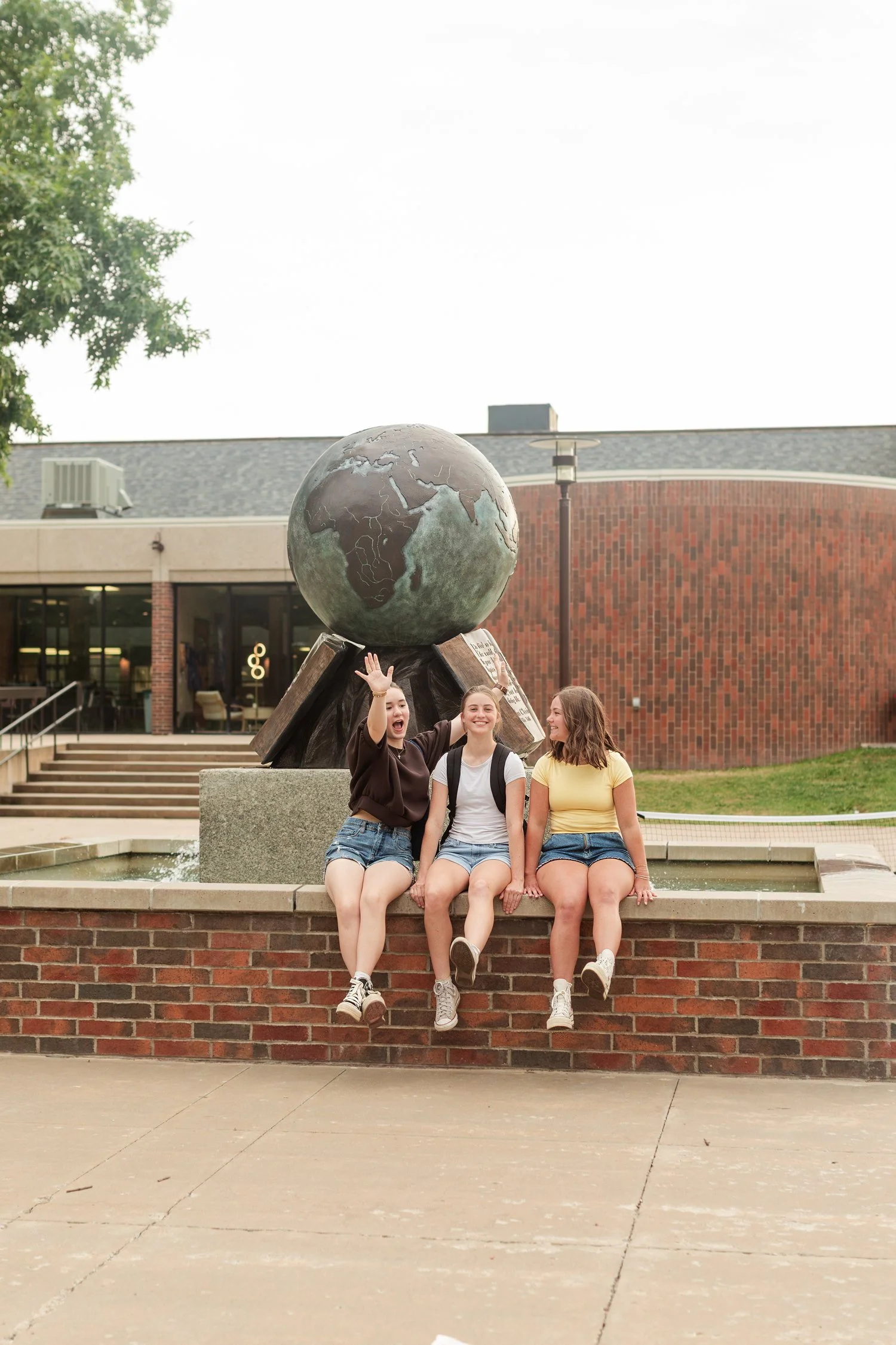 Three friends seated beneath a globe sculpture on campus.