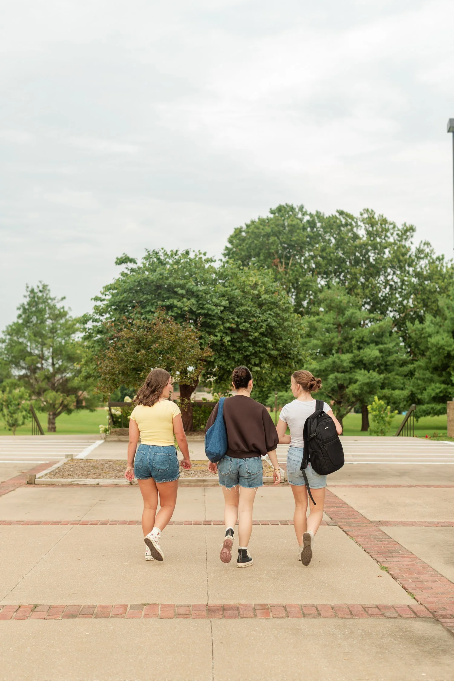 Three friends walking away along a path toward trees.