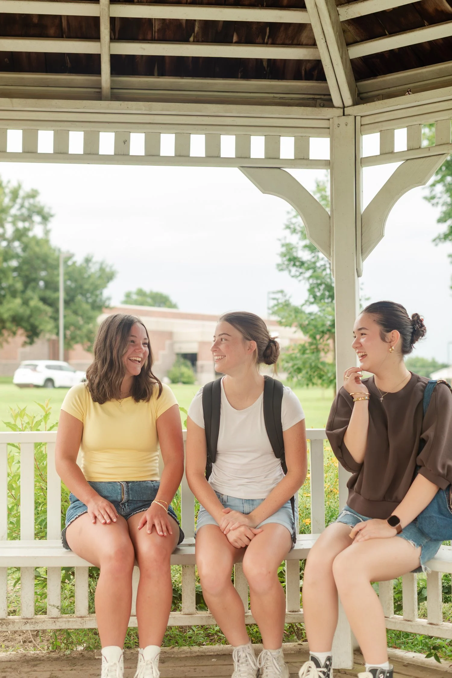 Three friends seated together inside a white gazebo.