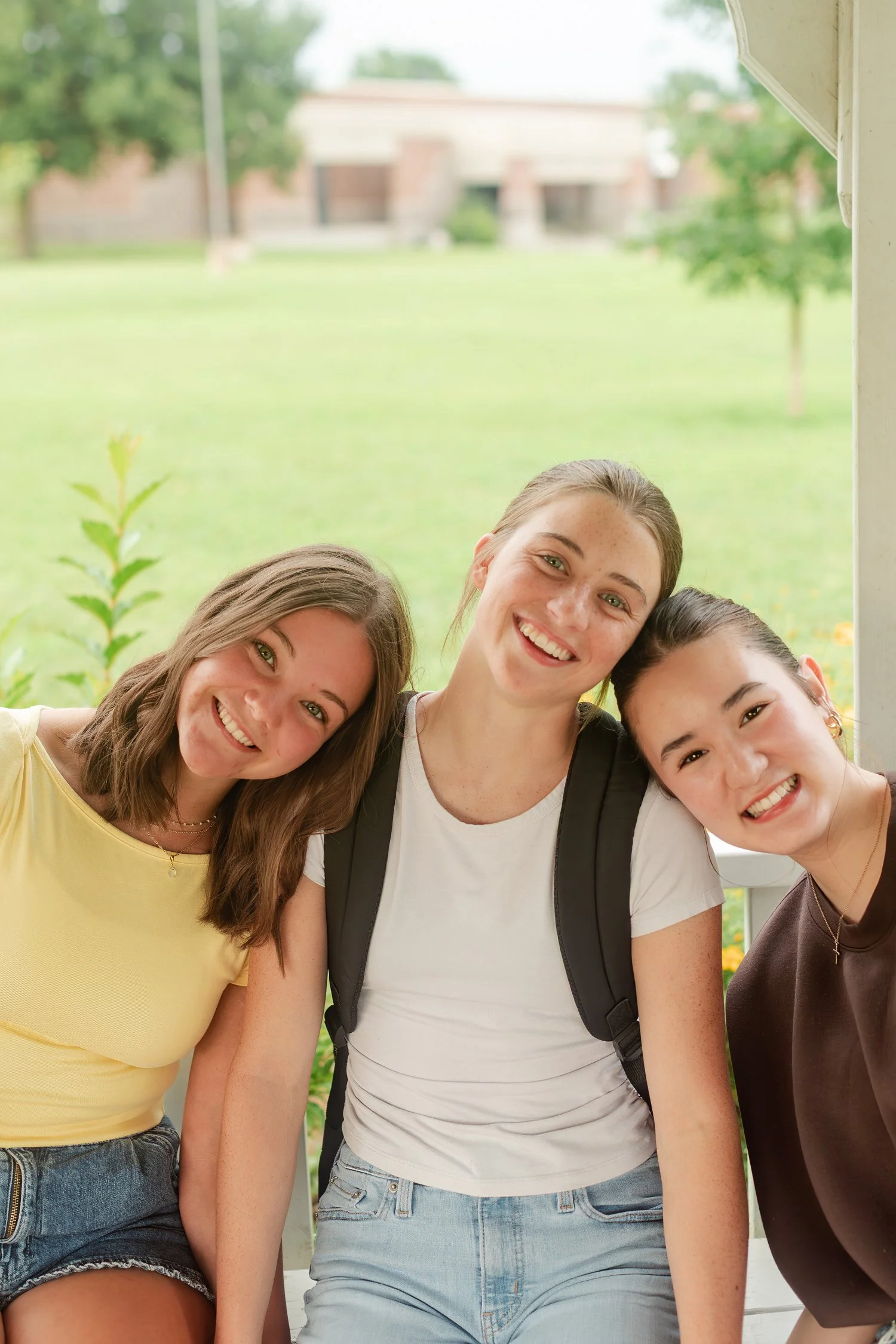 Three friends leaning their heads together outdoors.