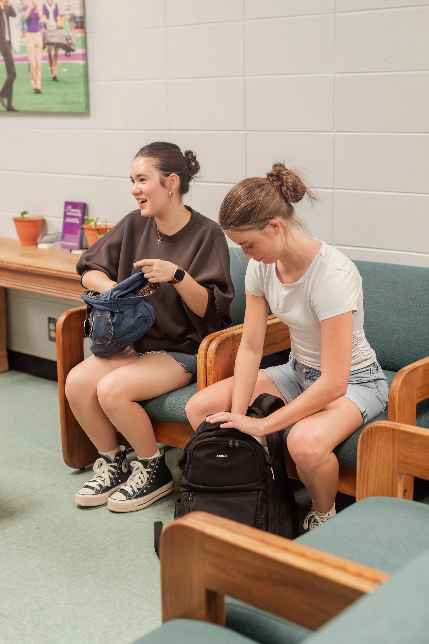 Two friends seated on a couch with backpacks in a campus lounge.