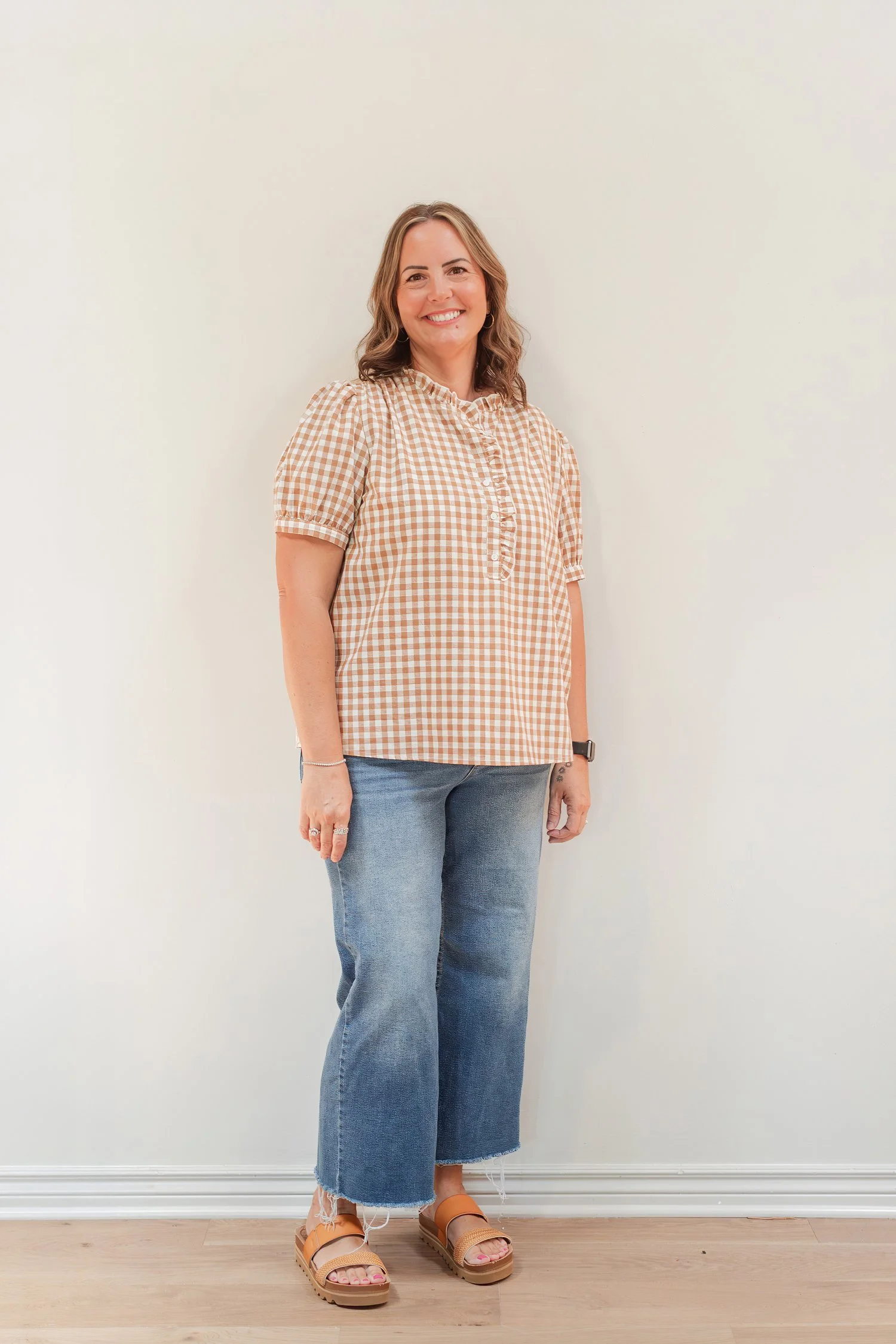 Real estate agent in a tan gingham top, cropped jeans and sandals standing against a white wall, full length headshot in Bolivar, MO